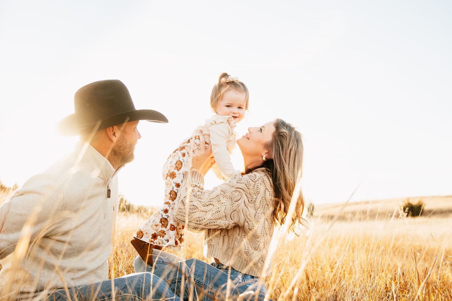 Family sitting together in golden field during sunset.