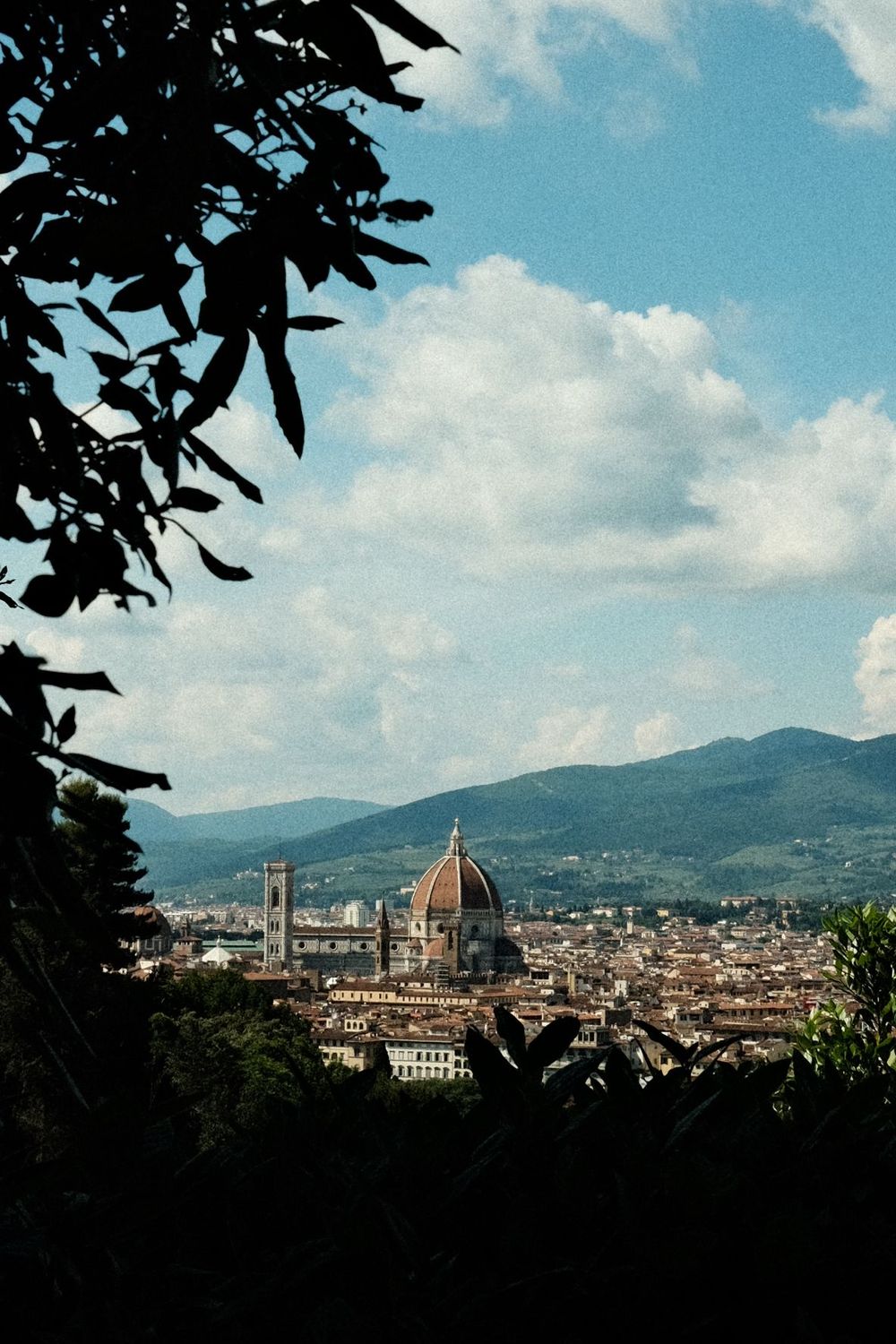 View of Florence Cathedral dome and cityscape framed by tree silhouettes against blue sky.
