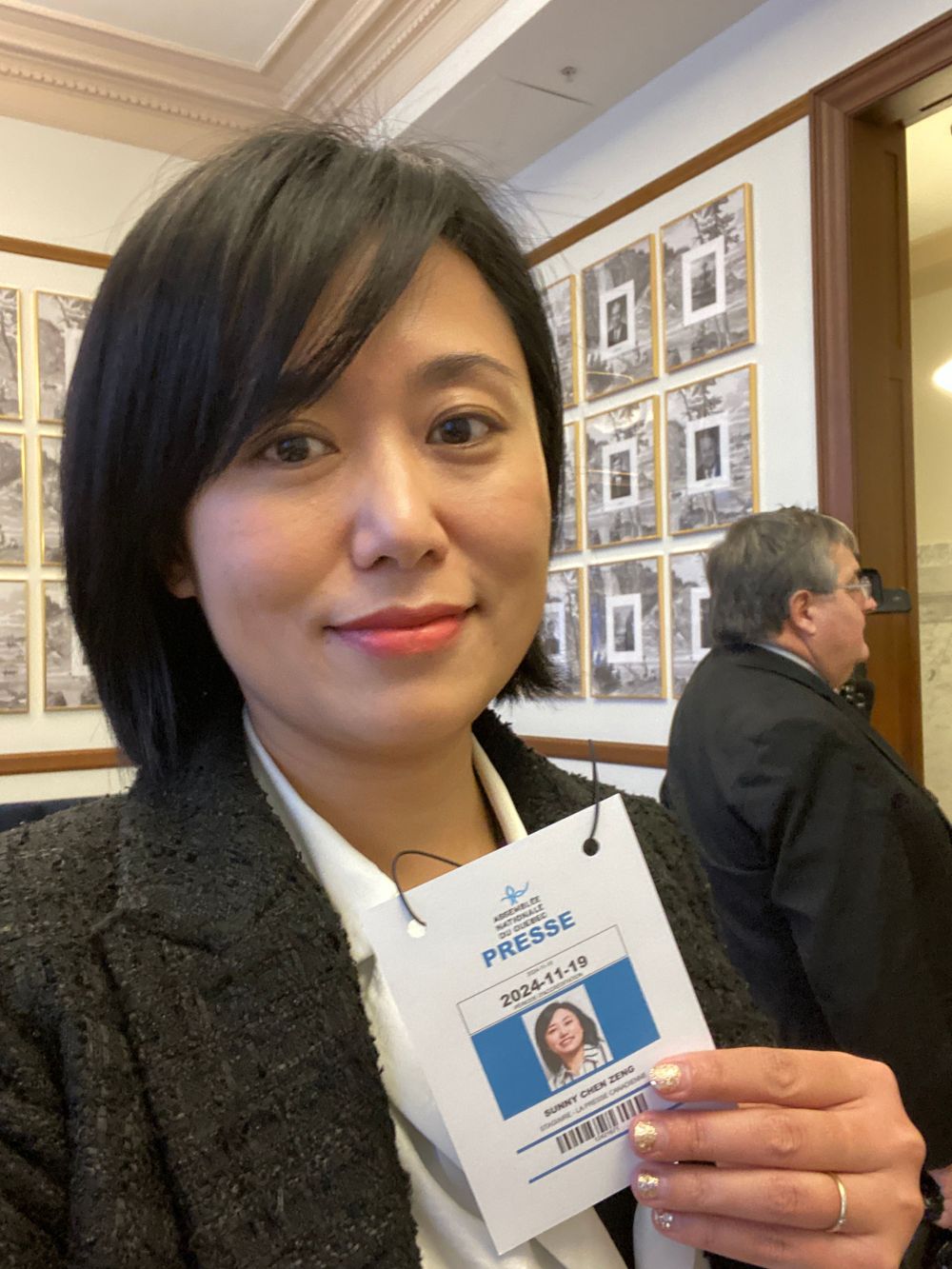 A press badge holder poses inside a professional building hallway.