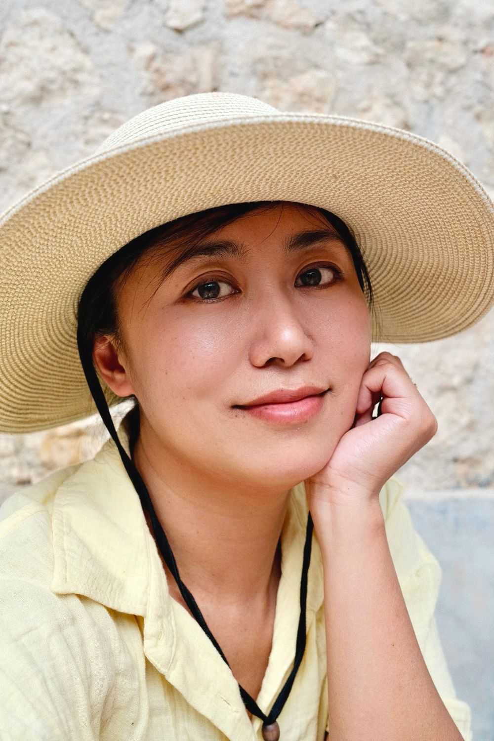 Portrait of woman in straw hat against stone wall background.