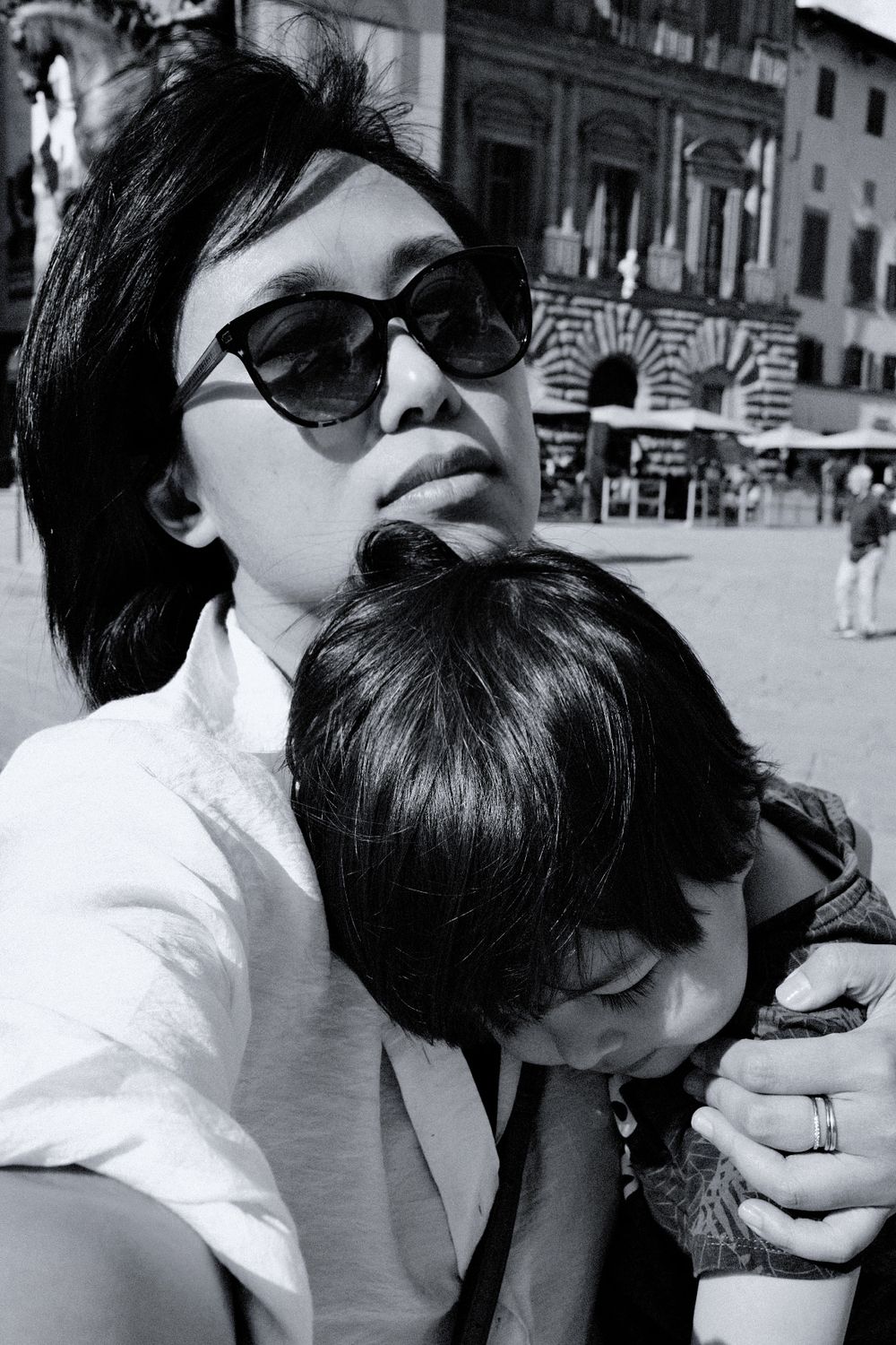 Casual black and white street portrait in sunglasses against urban backdrop.