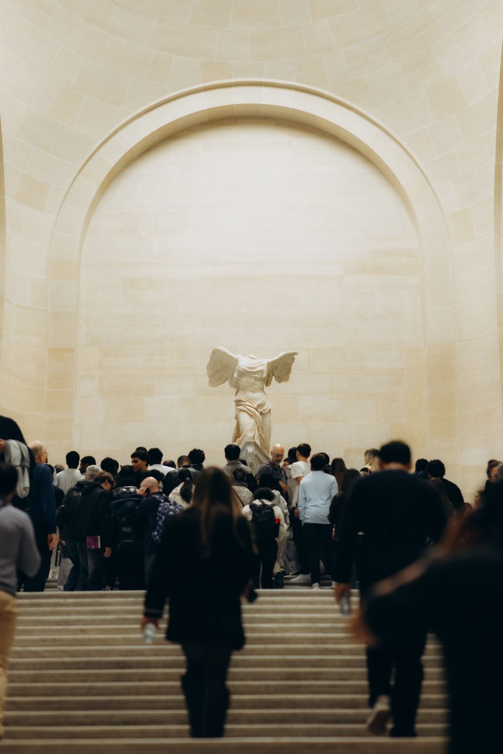 Crowds of tourists climb the grand staircase toward the Winged Victory of Samothrace sculpture at the Louvre Museum in Paris.