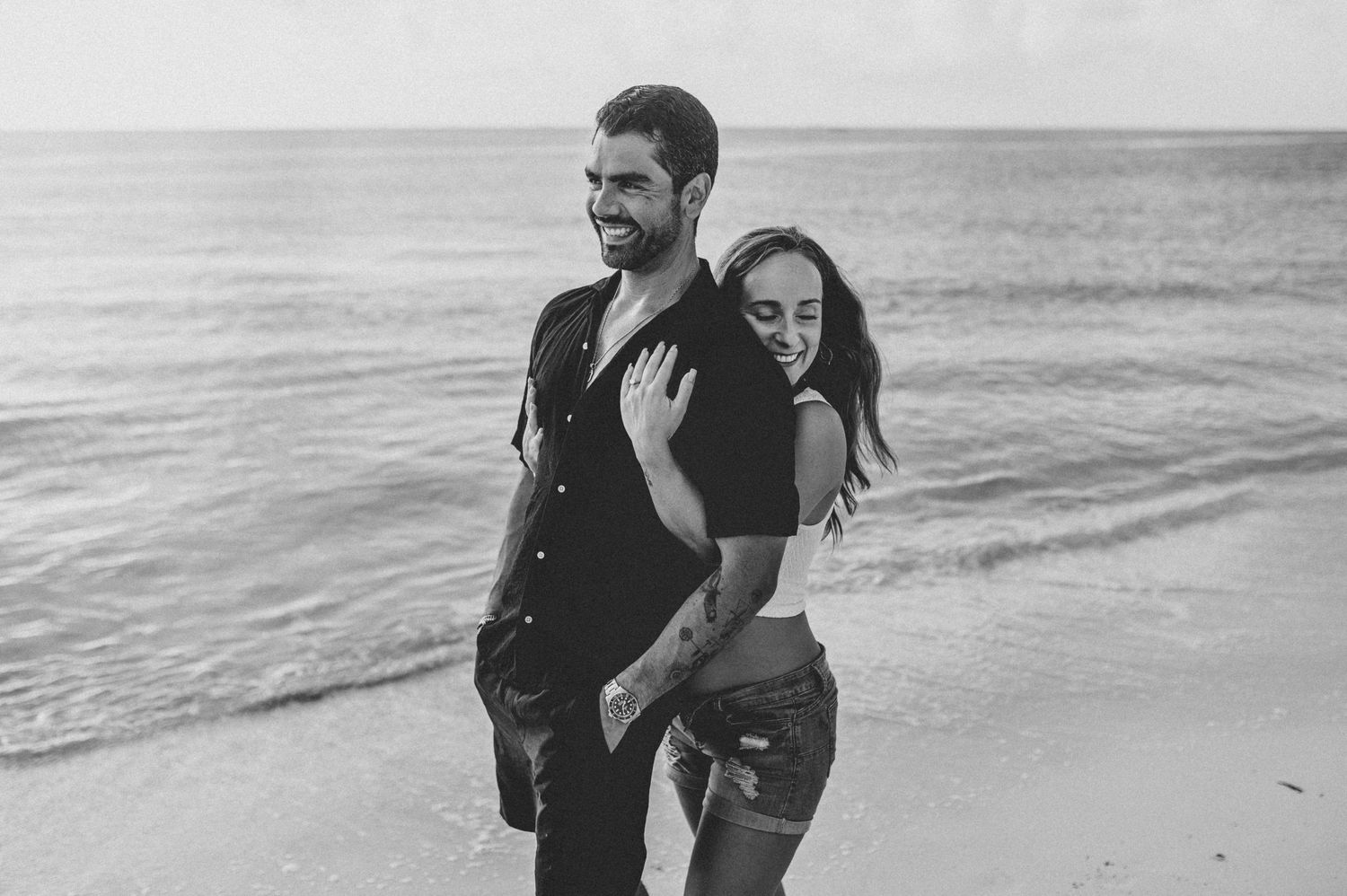 A couple laughs together in black and white while embracing on a beach with ocean waves in the background.
Lifestyle photographer Mexico