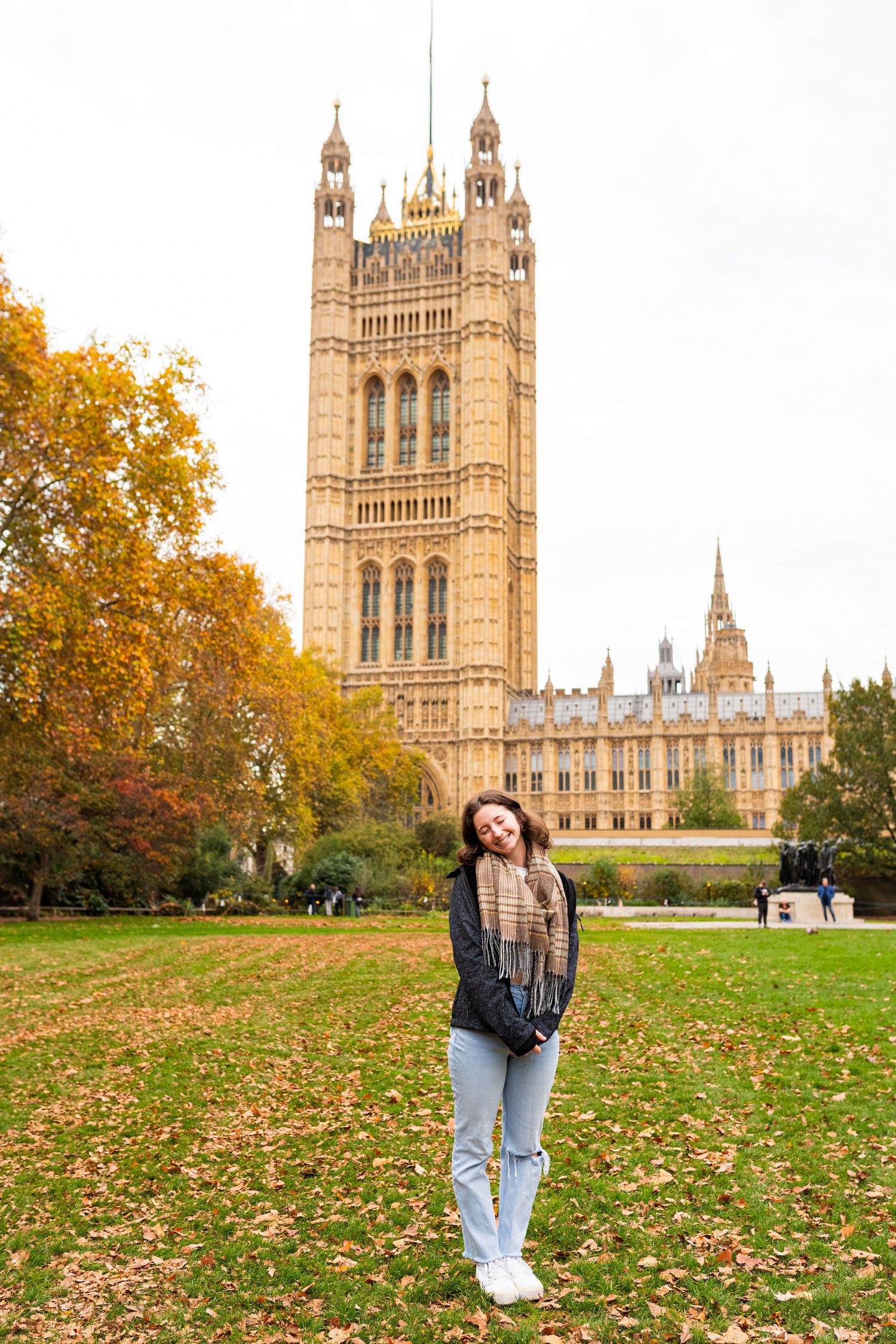 Autumn scene at Westminster Palace with fallen leaves on lawn and historic Gothic architecture in background.