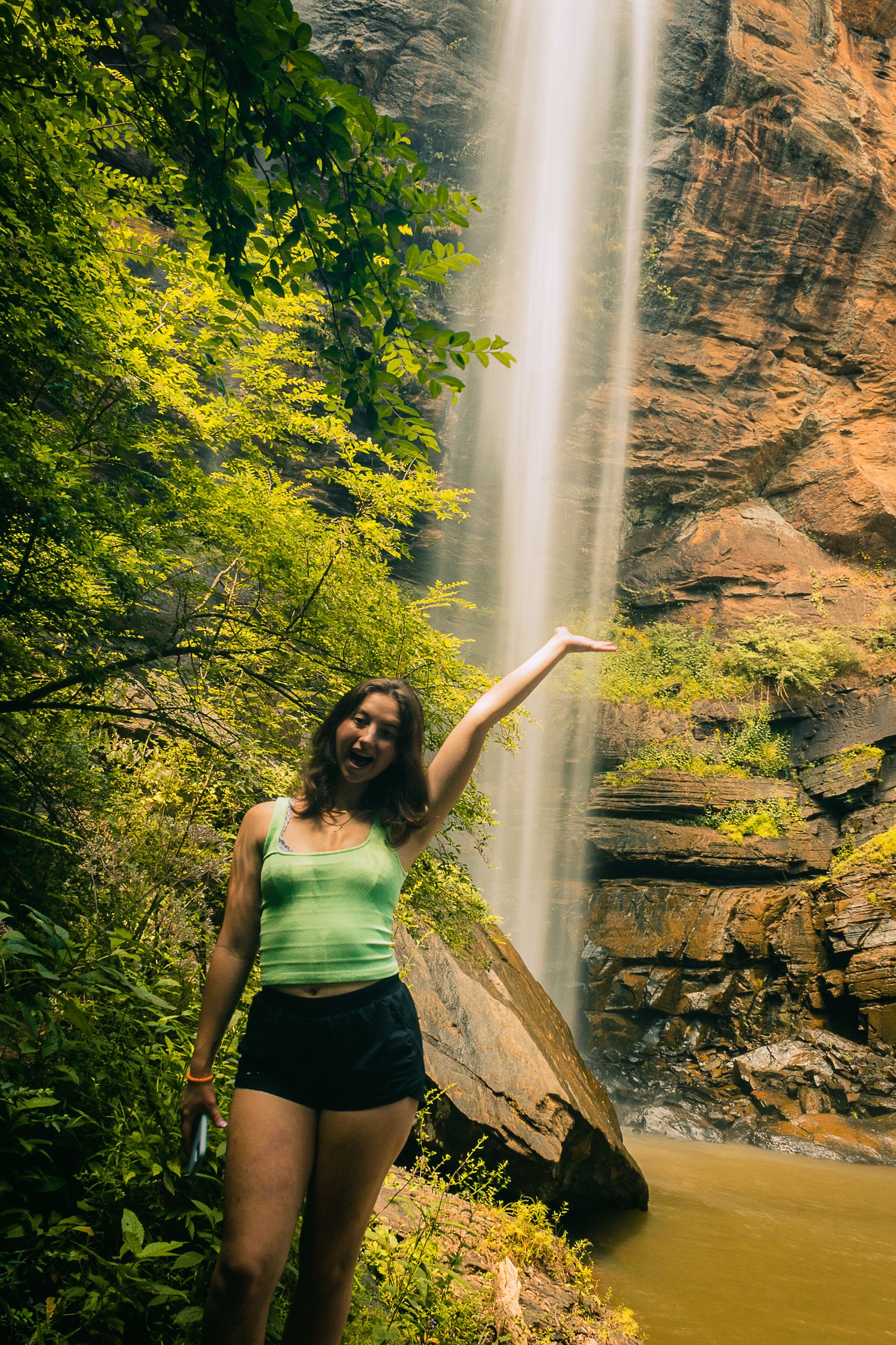 A majestic waterfall cascades down orange rocky cliffs surrounded by lush green foliage.