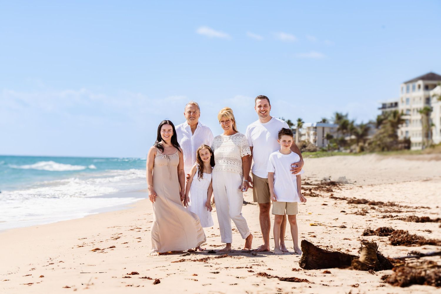 Family in coordinated white outfits poses together on beach.