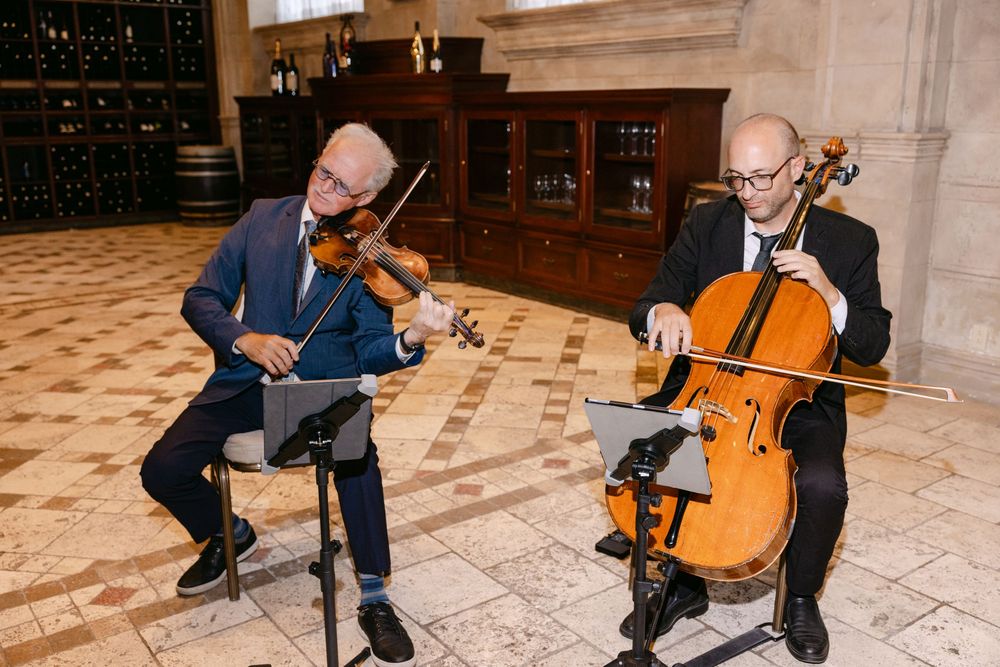 Two musicians performing classical music together with violin and cello in an elegant stone interior.