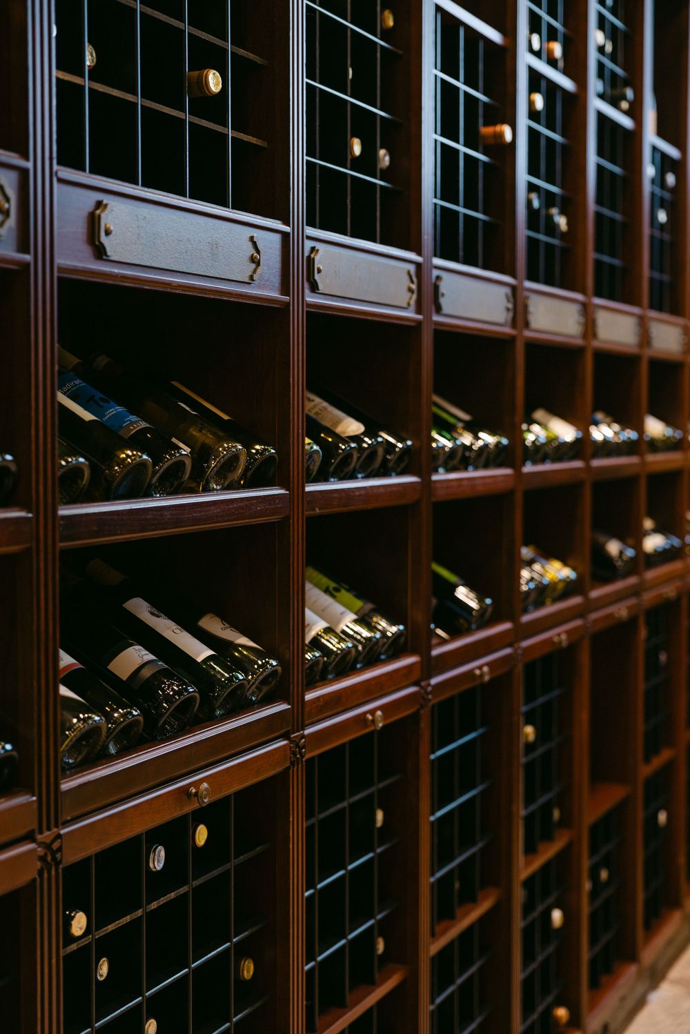 Rows of wine bottles stored in elegant wooden racks illuminated with ambient lighting in a luxury wine cellar.
