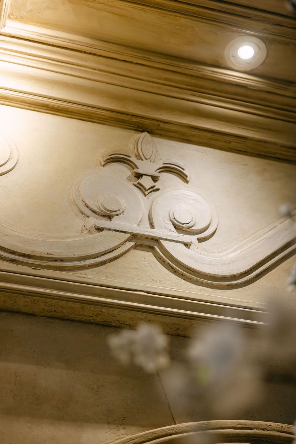 Ornate vintage crown molding detail with decorative flourishes illuminated by a ceiling light.