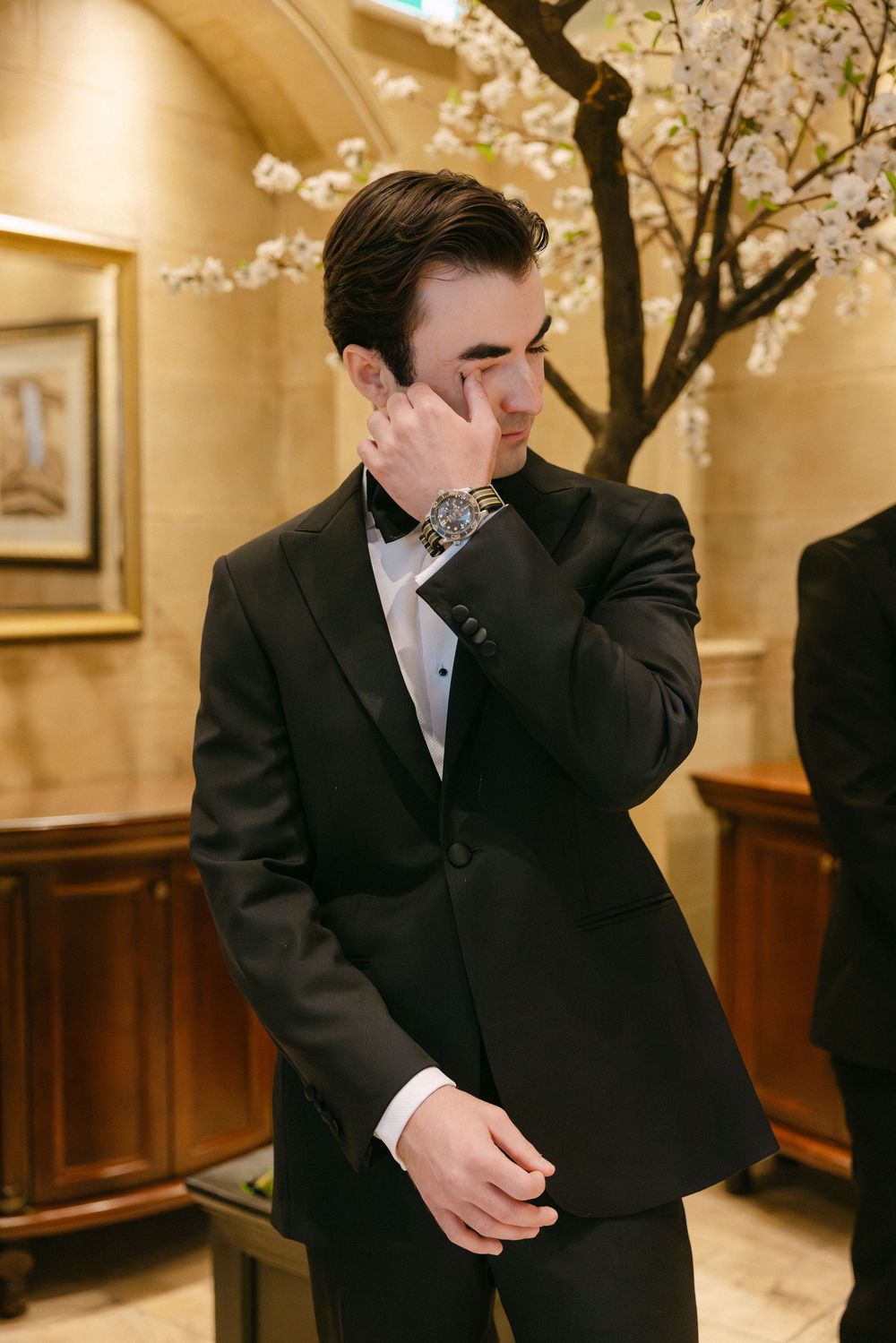 Emotional moment in black tuxedo with cherry blossoms blooming in elegant indoor setting.