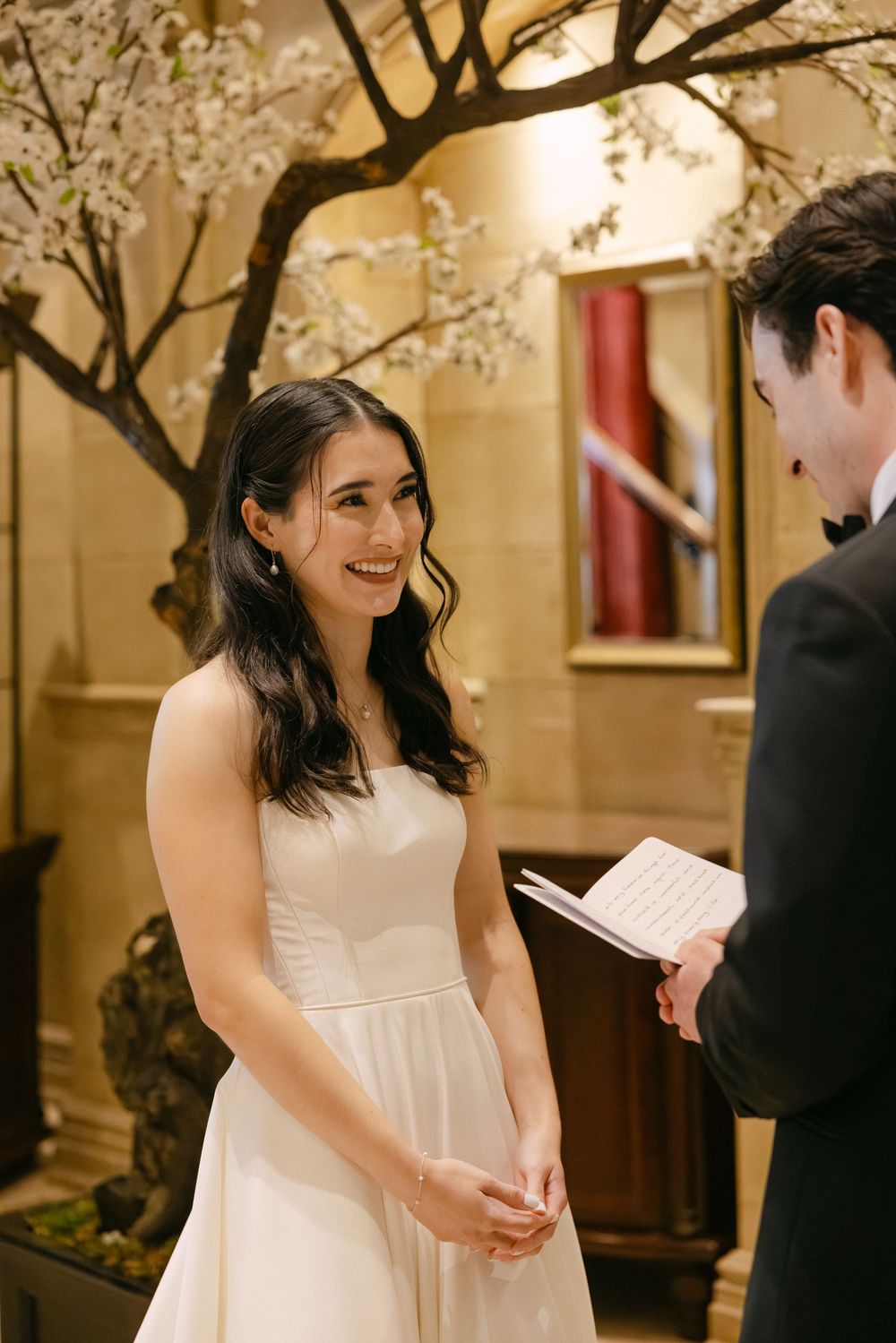 A couple exchanges vows during an intimate indoor wedding ceremony under a beautiful blooming cherry blossom tree.