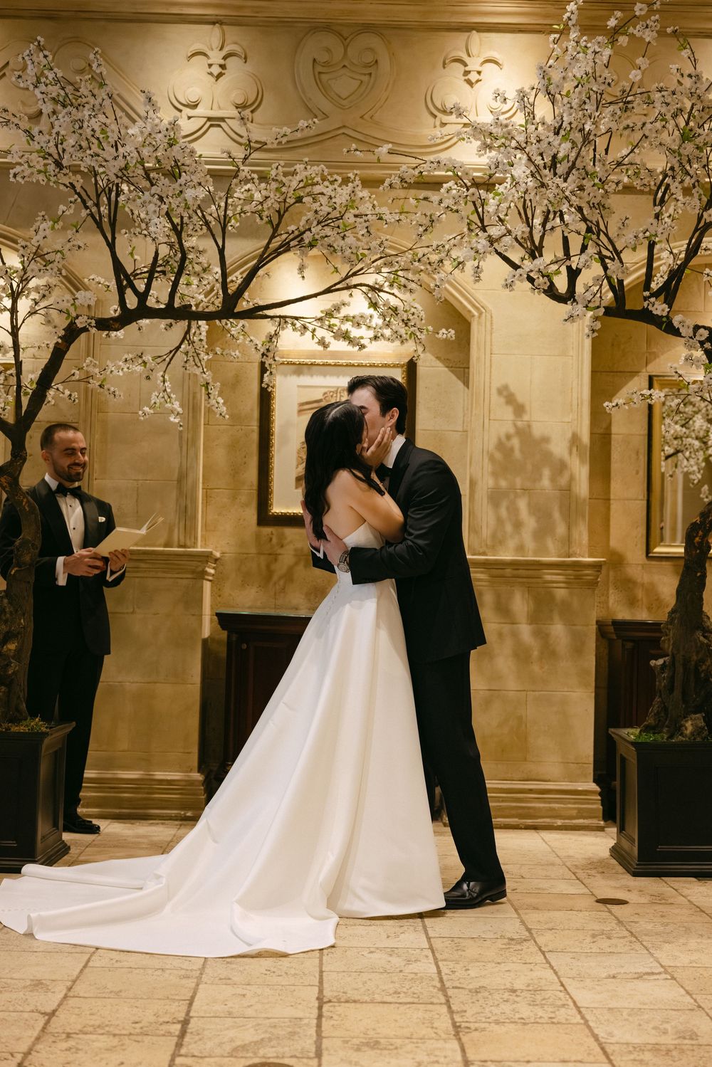 Indoor wedding ceremony with ornate gold walls and decorative cherry blossom trees creating a romantic atmosphere.