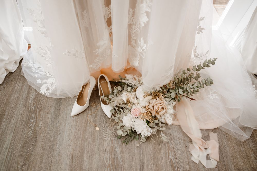 Wedding dresses displayed with delicate floral arrangements and cream colored heels on hardwood flooring.