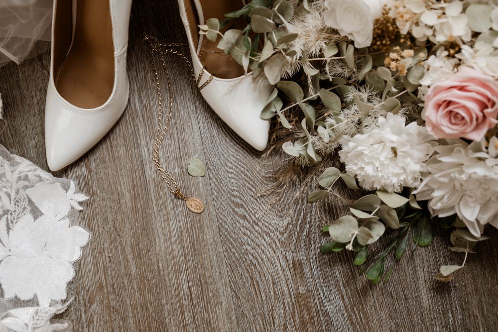 Wedding details including pink roses, white flowers, bridal shoes and eucalyptus on rustic wood background.