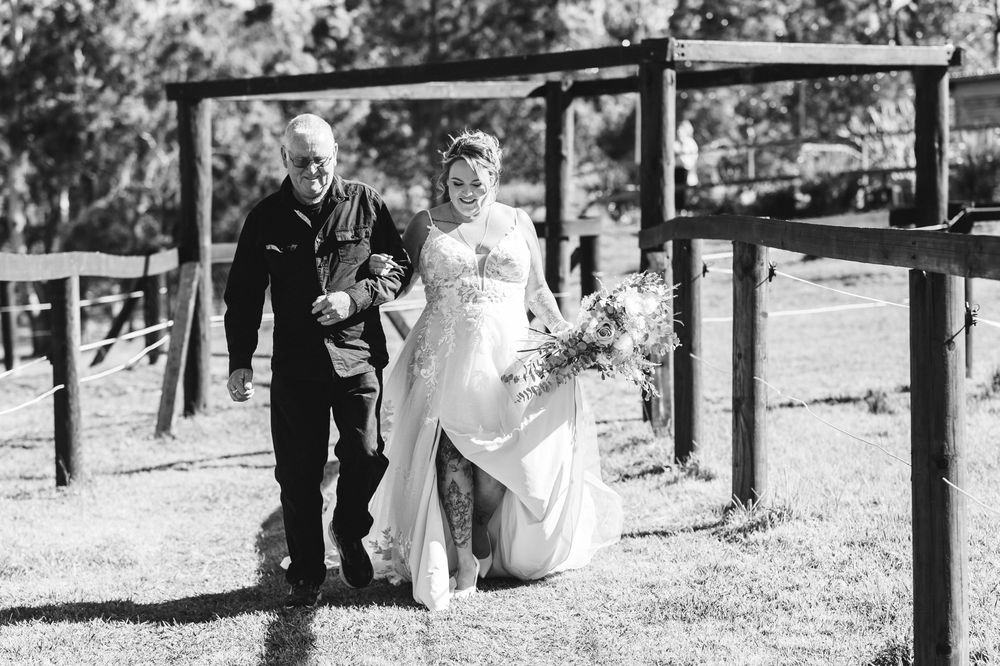 A romantic couple walks under rustic wooden beams outdoors during their wedding celebration.