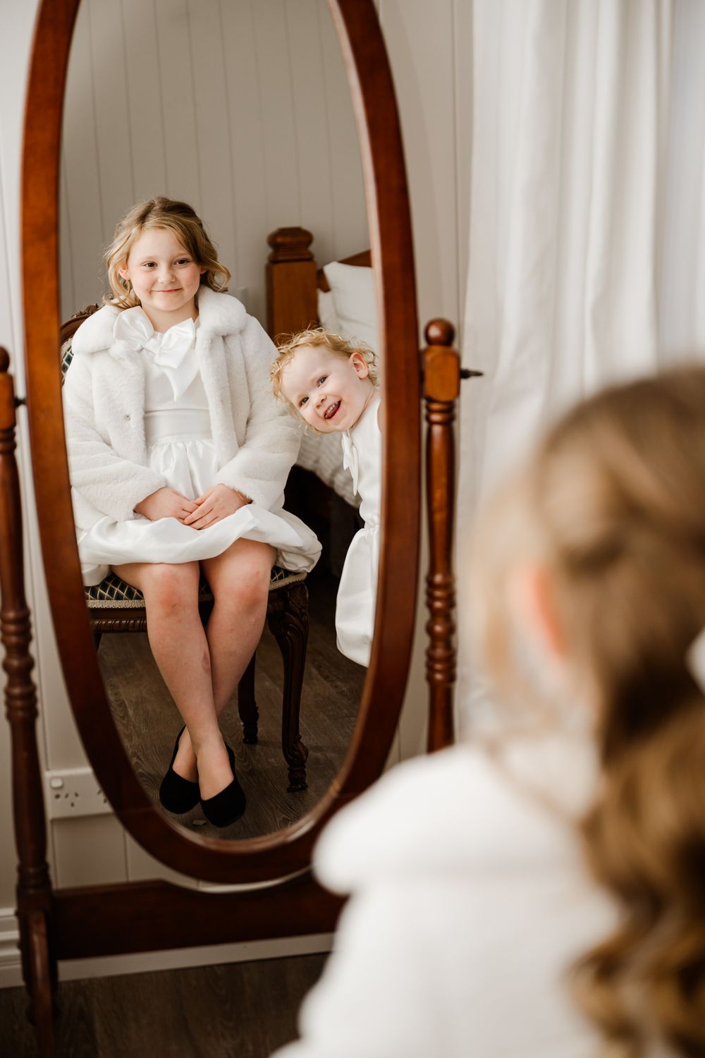 Ornate wooden mirror on white walls reflects warm ambient light in an interior setting.