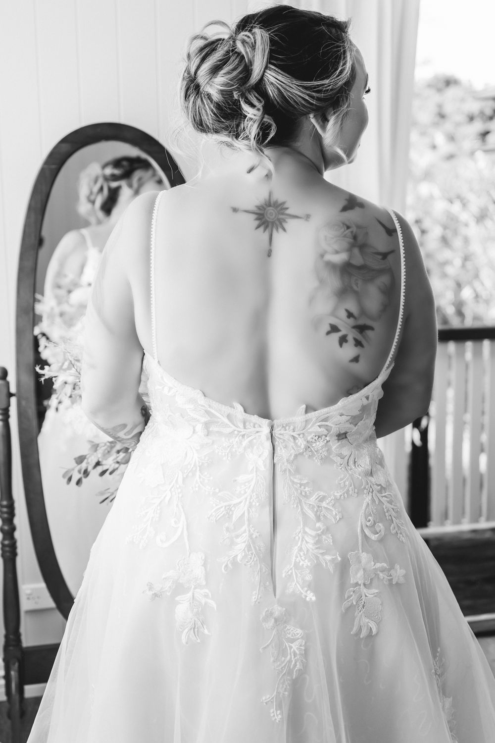 Three bridesmaids in white lace dresses showing intricate back details and floral embellishments at a formal event.