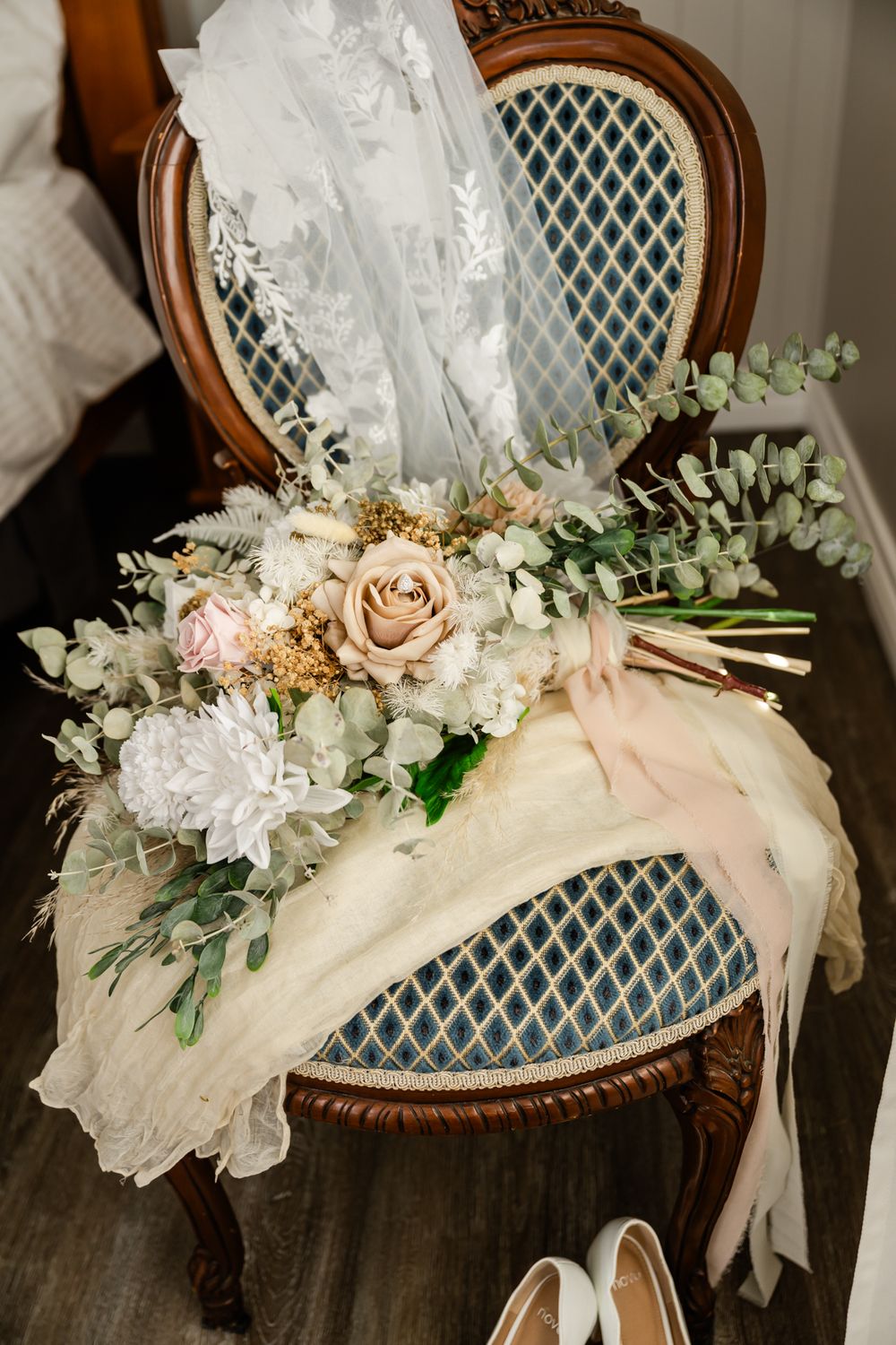 Romantic wedding floral arrangement with blush roses and white flowers draped on an antique chair with lattice backing.