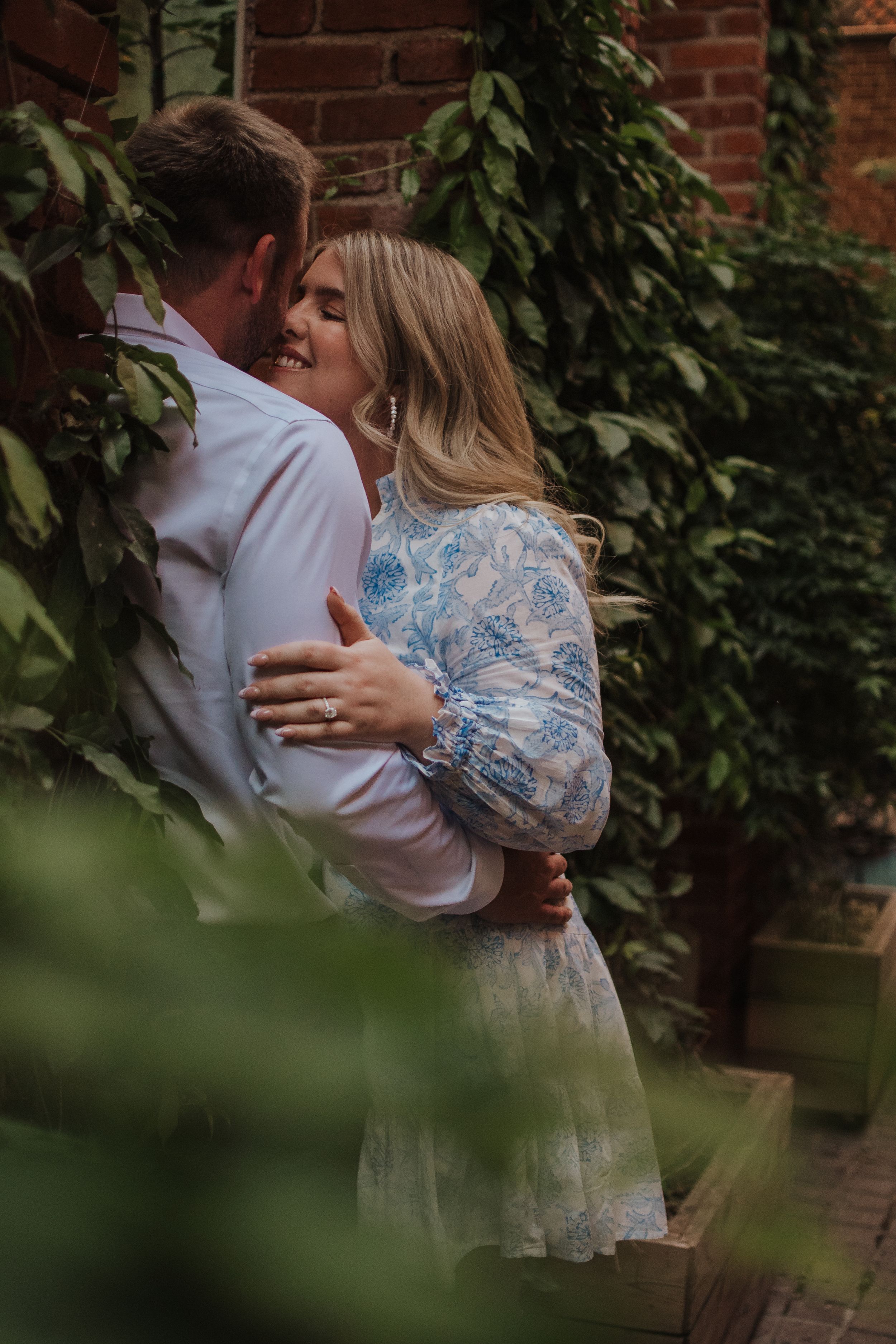 Romantic engagement photoshoot sequence with couple embracing by ivy-covered brick wall in garden setting.