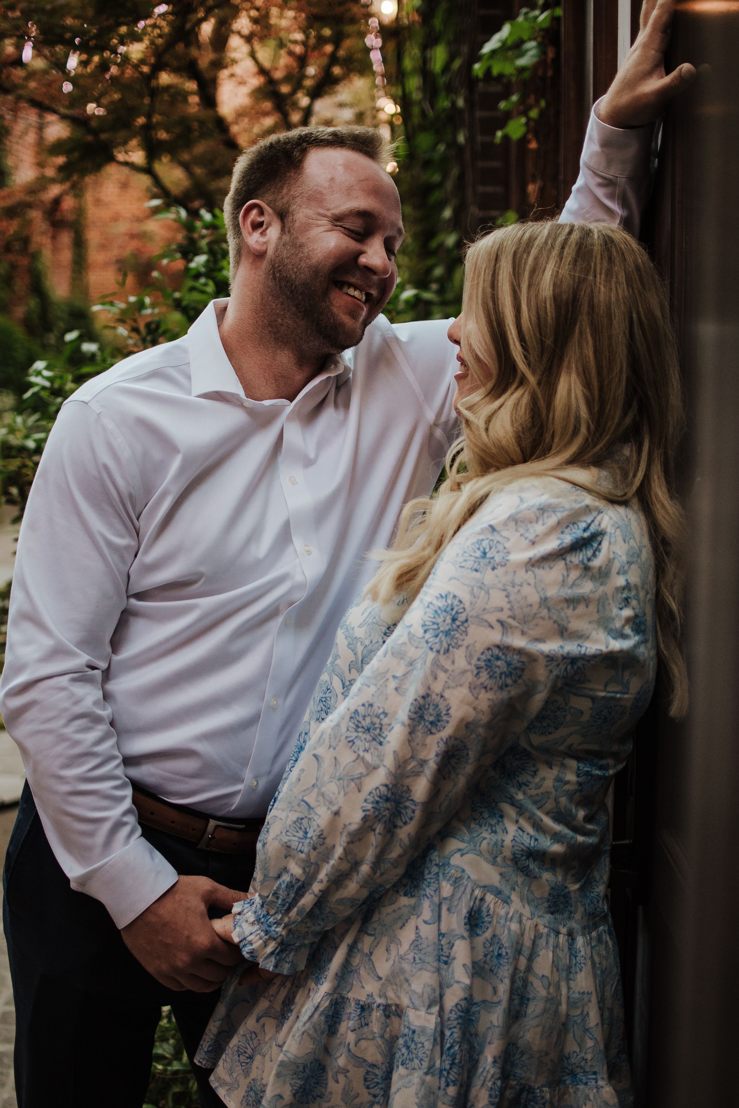 A couple in a white shirt and floral dress share intimate candid moments during an outdoor photo session at sunset.