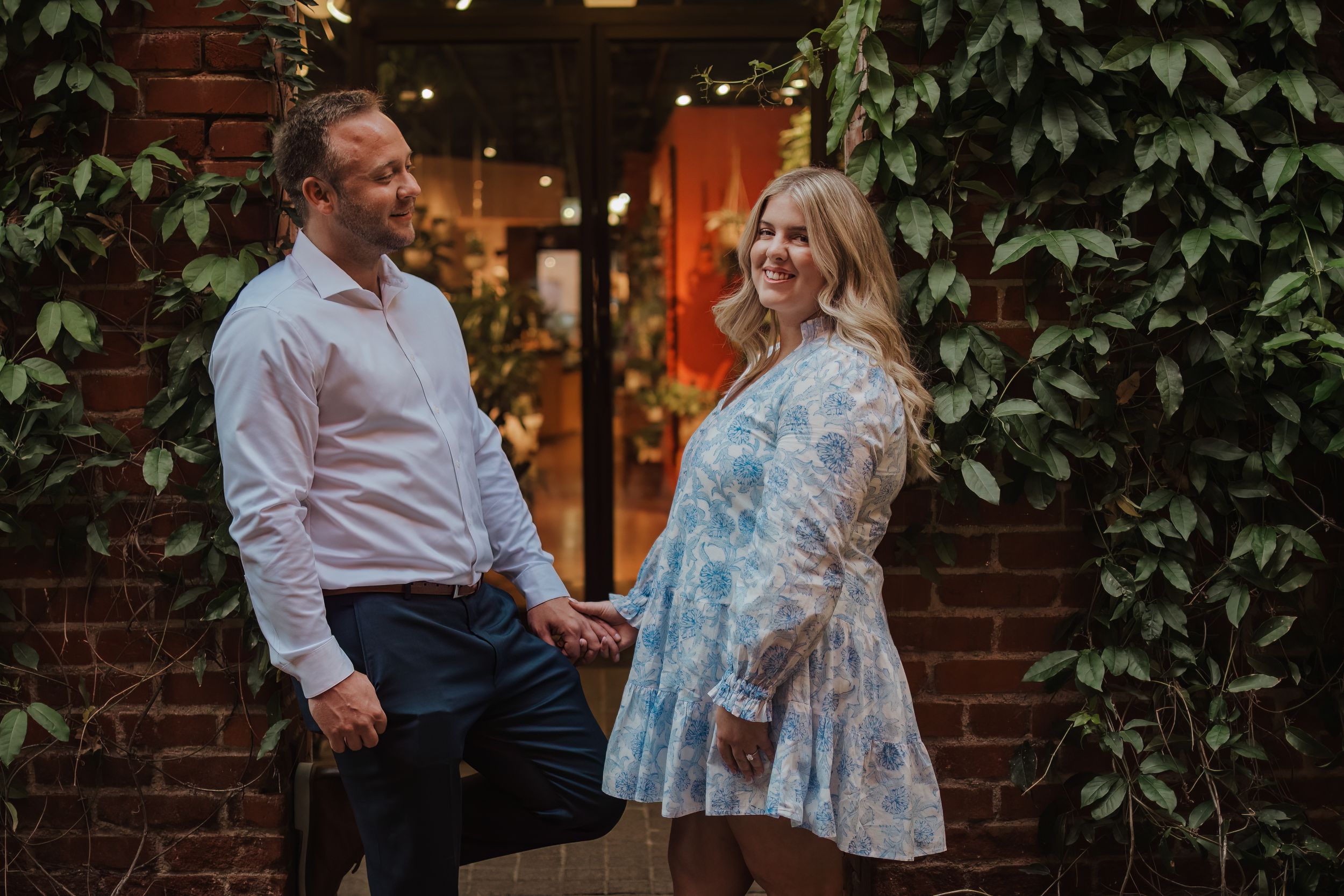 A couple shares a moment together outdoors in front of a brick wall with lush green vines.