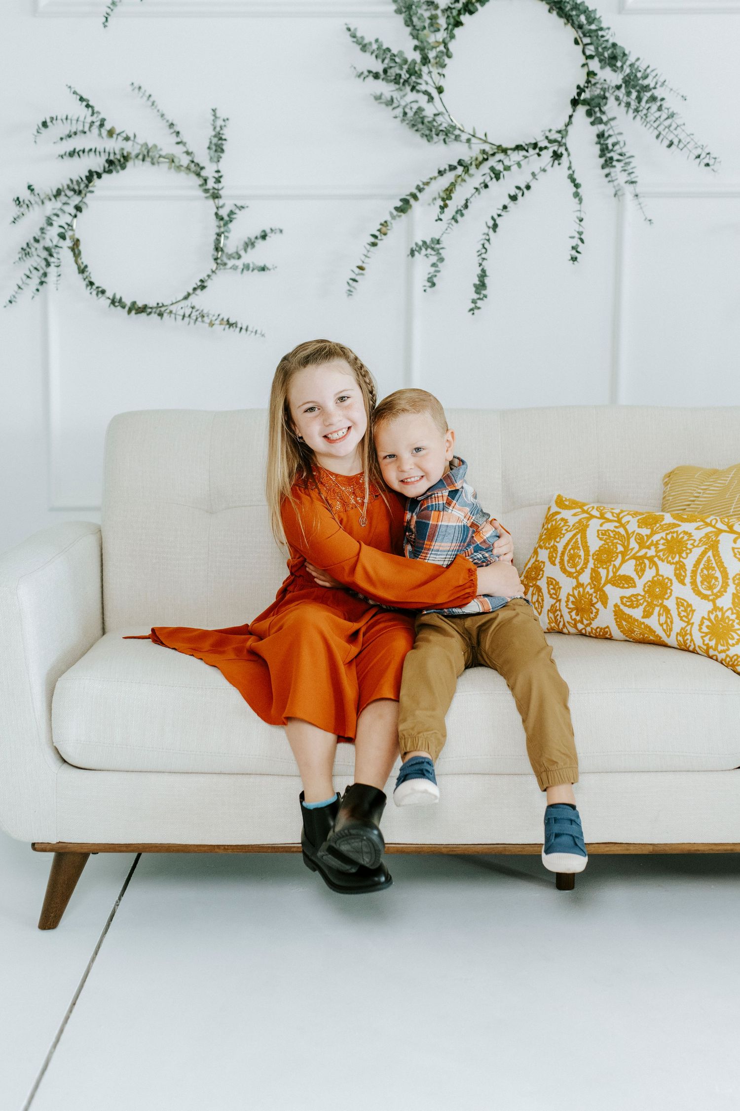 A cozy family scene on a modern white couch with orange and yellow accents and delicate greenery above.