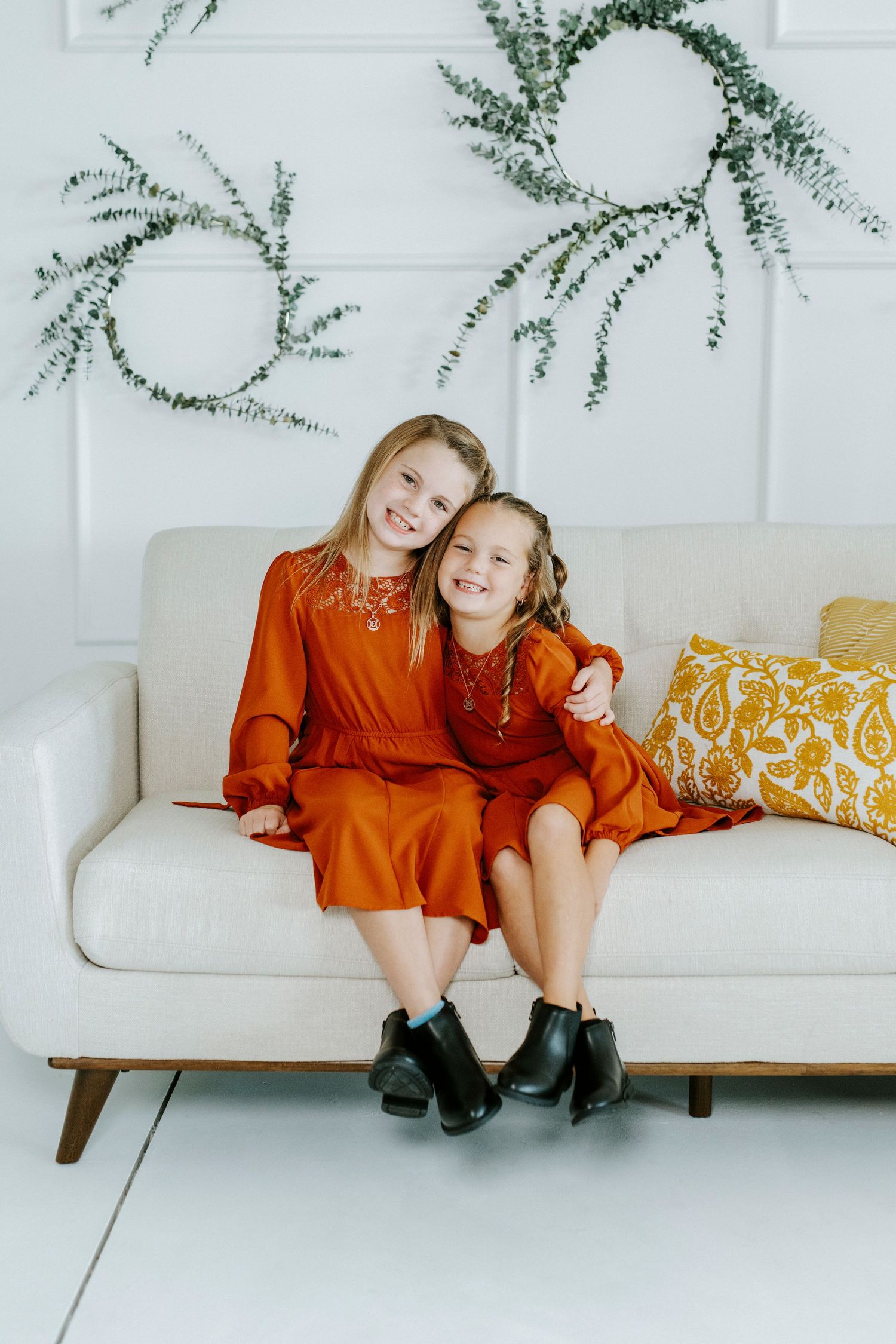 Two people wearing orange dresses sit close together on a modern white couch with yellow patterned pillows.