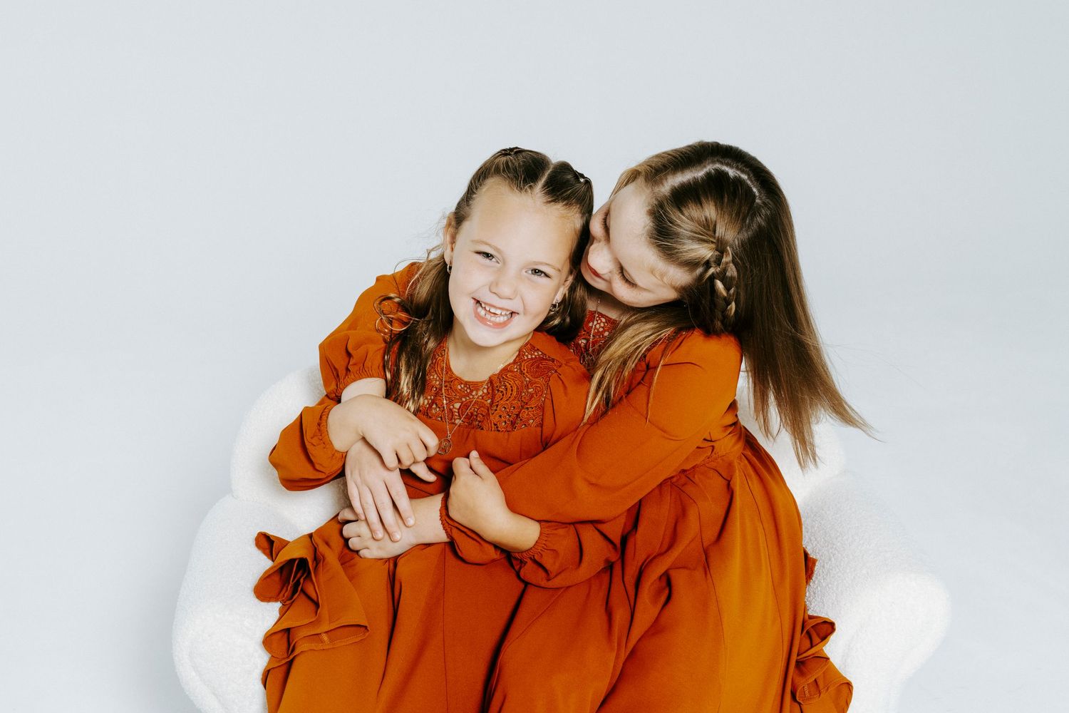 Two people in matching burnt orange sweaters laugh and embrace against a light background.