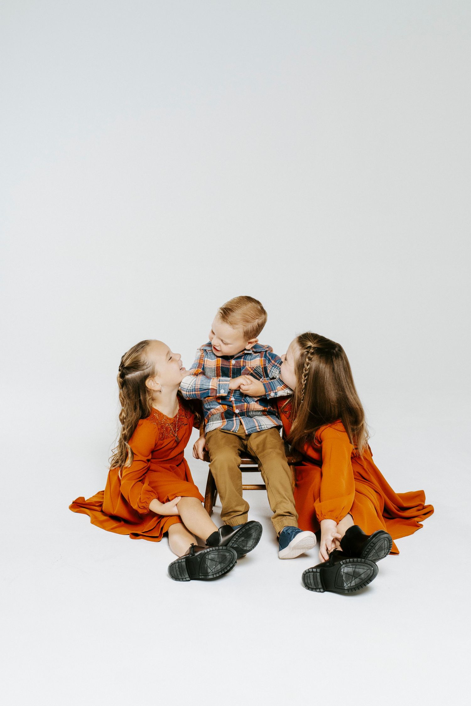 Touching sequence of children in orange shirts and jeans sitting and playing together on white background.
