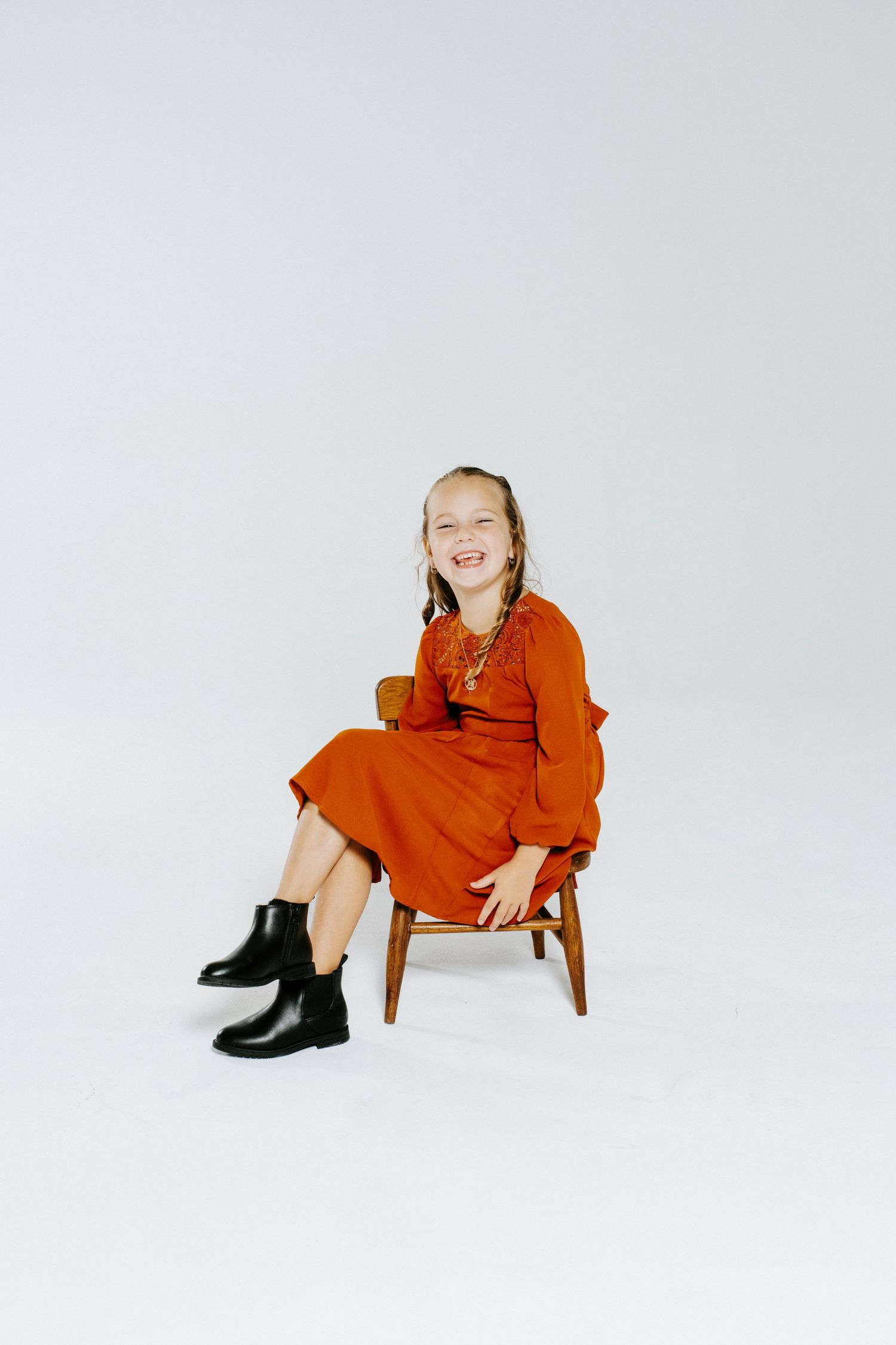 A figure in an orange dress sits and poses playfully in various positions against a white backdrop.