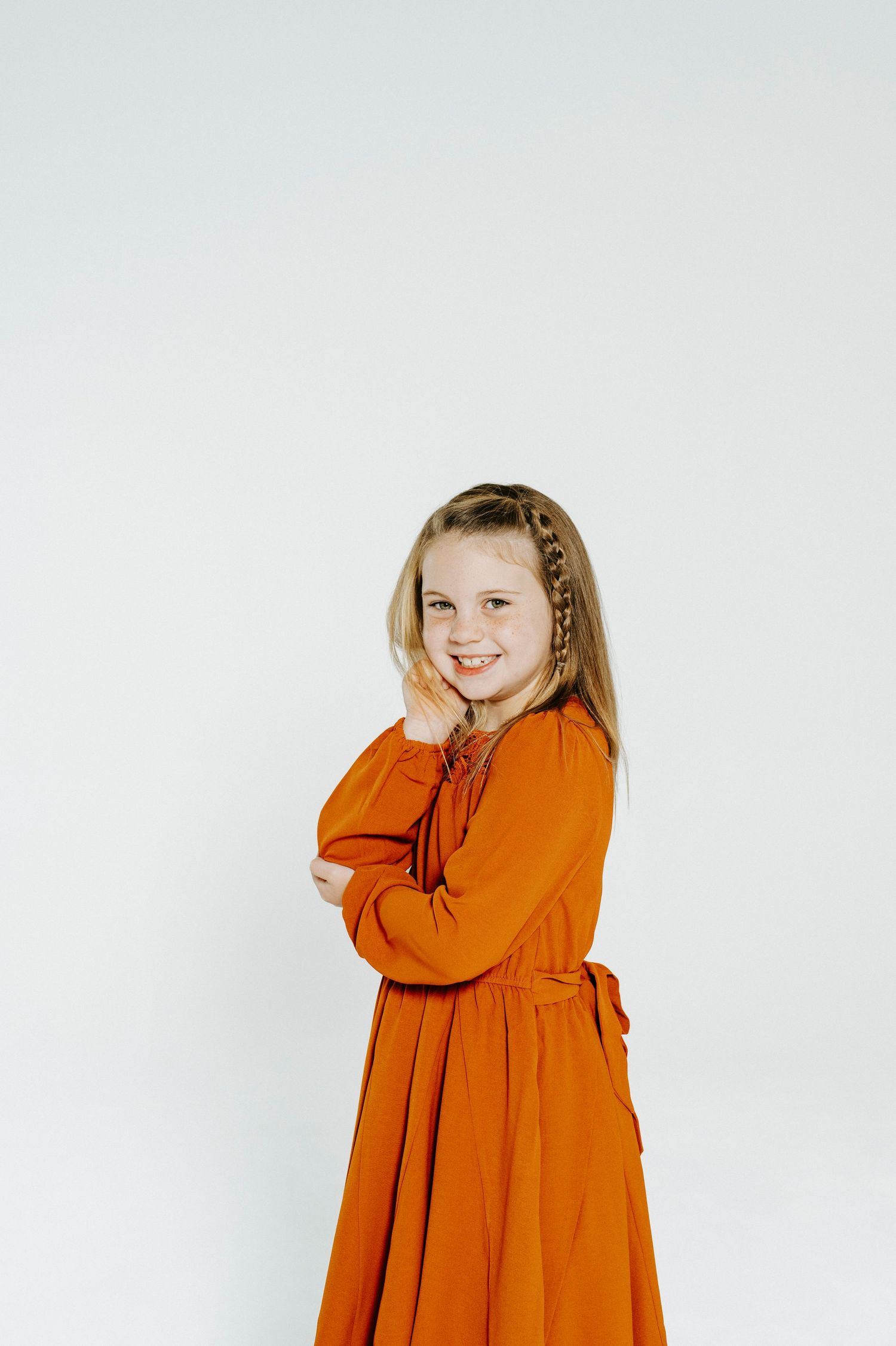 Four sequential photos show a child in a vibrant orange dress displaying playful poses against a white background.