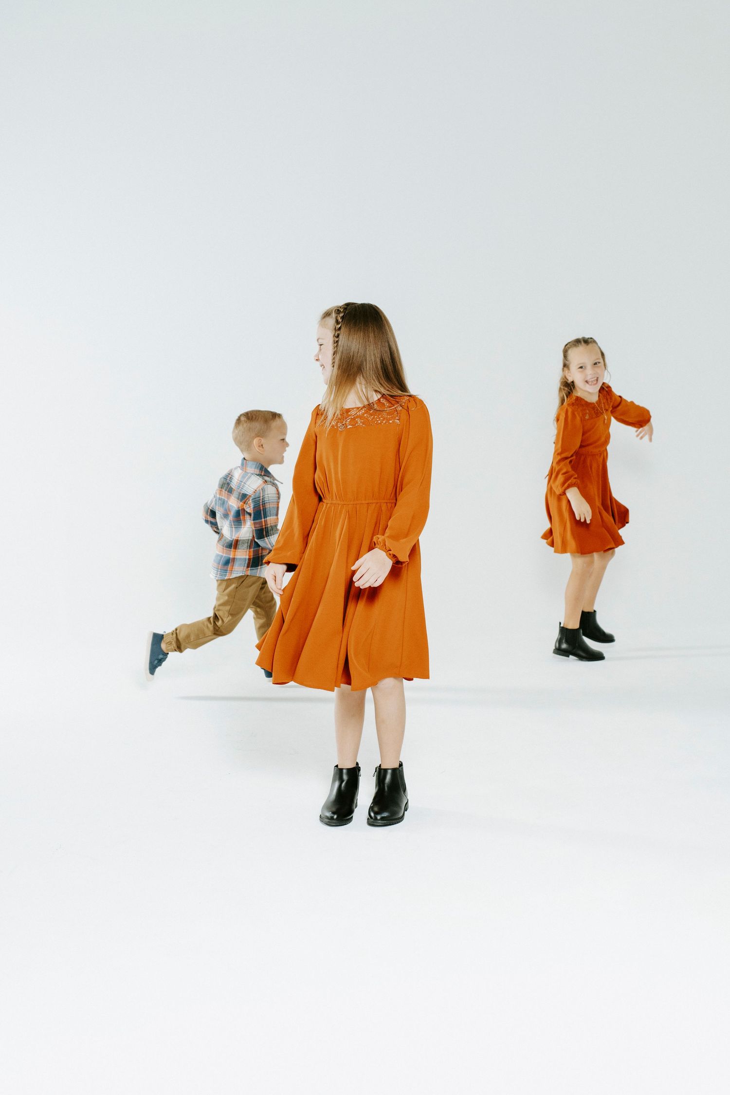 Two figures stand together on a white backdrop wearing contrasting orange and plaid outfits in a minimalist photoshoot.