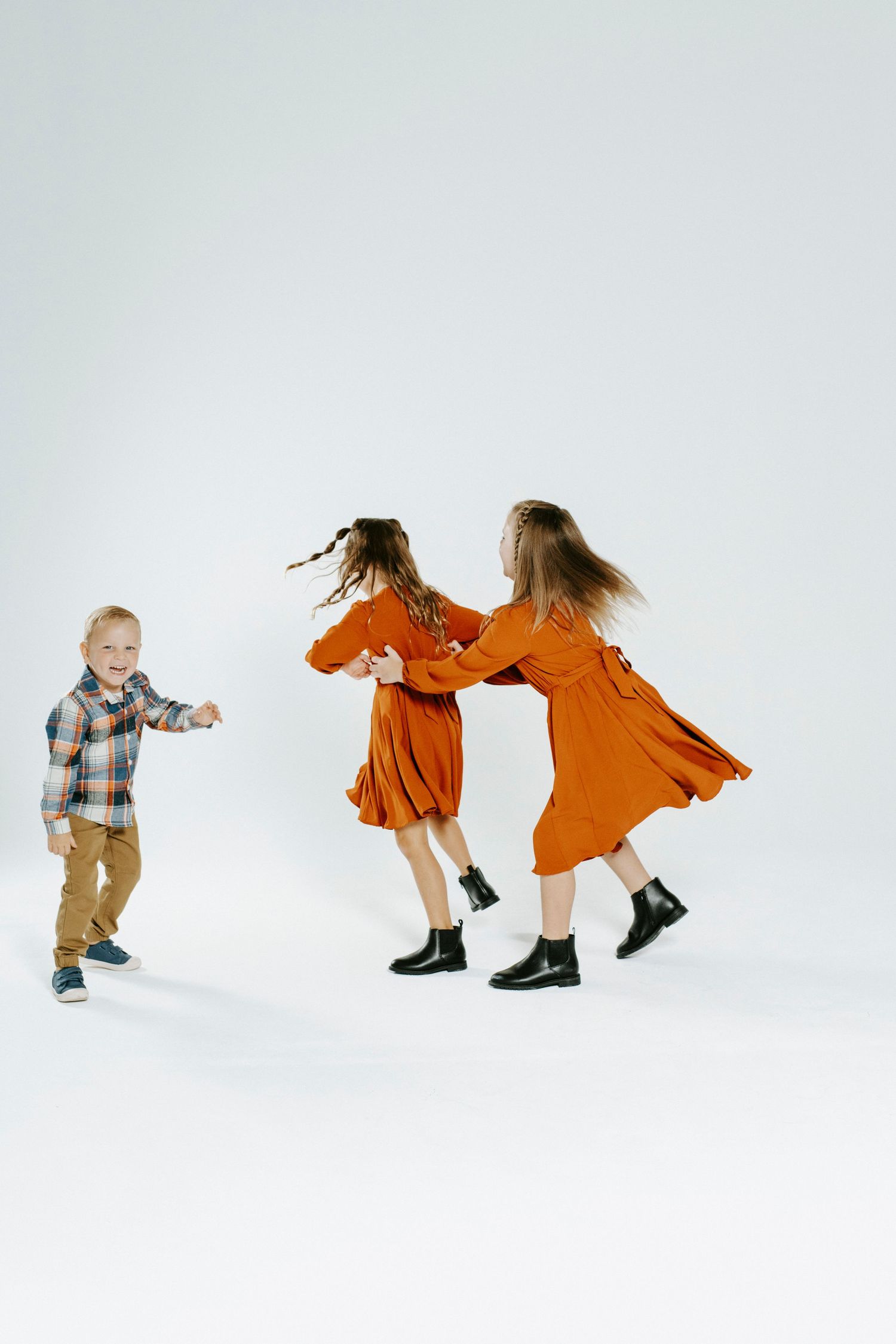 Sequence of photos showing two children playing and running around in a bright white photo studio setting.