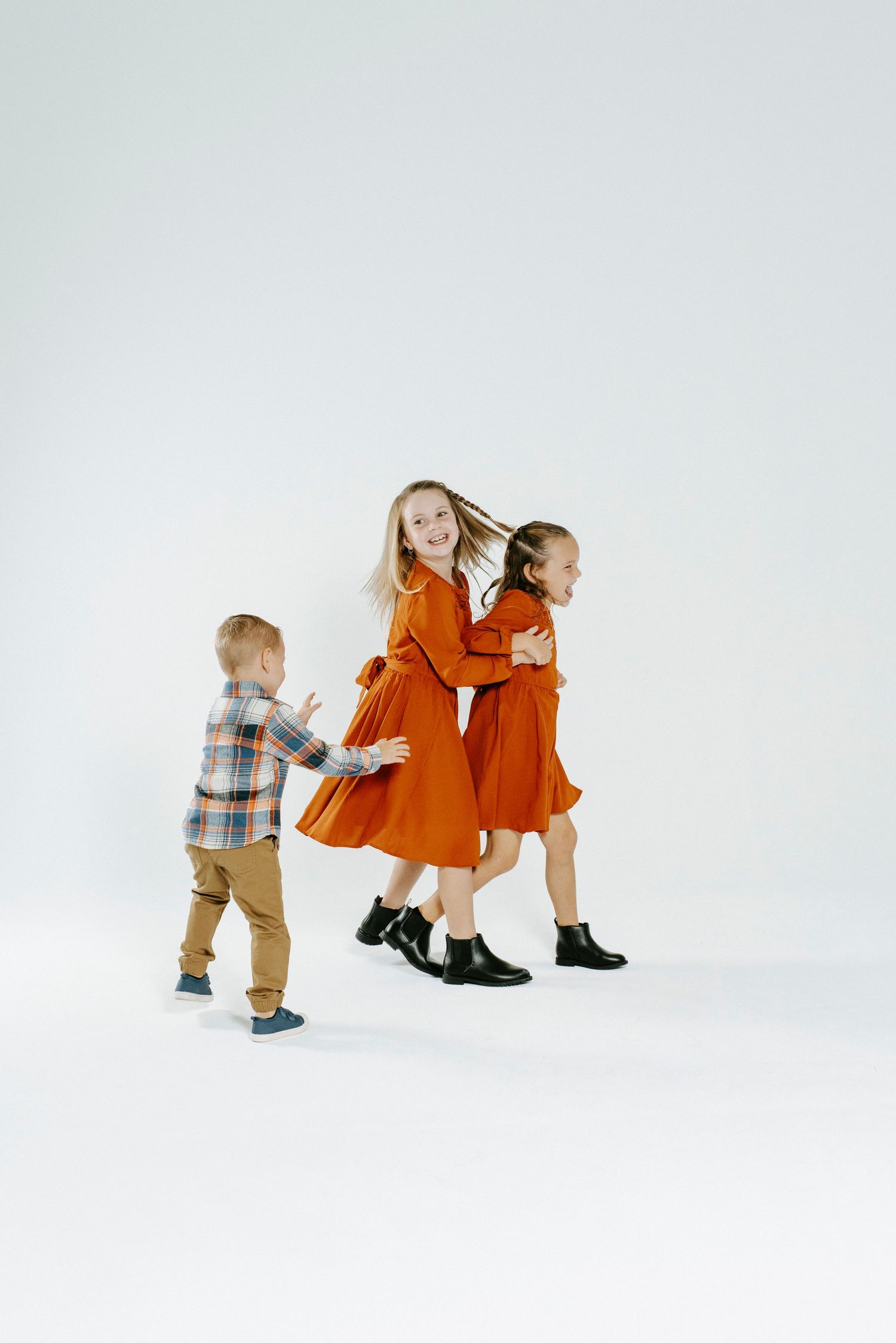 Children play together in a sequence of candid shots wearing orange and plaid outfits against a white background.