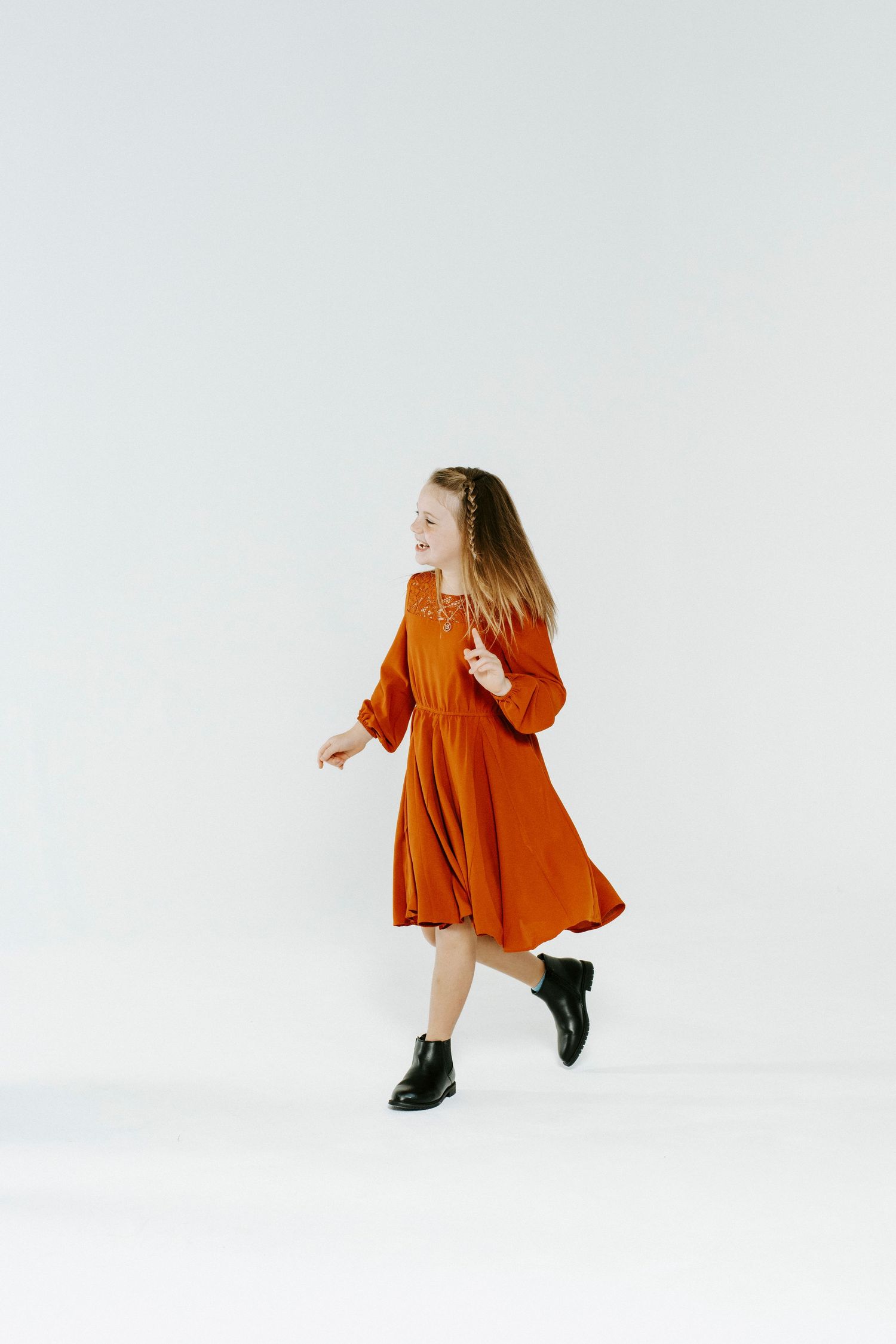 A figure in a vibrant orange dress twirls and moves expressively against a minimalist white background.