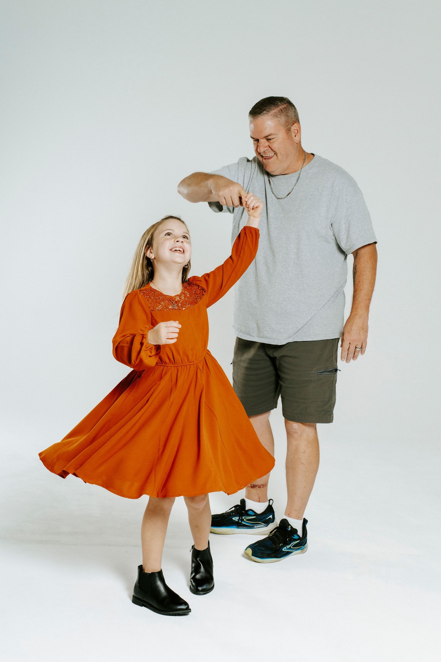 Parent and child in grey and orange outfits share a playful dance moment against a minimalist white background.