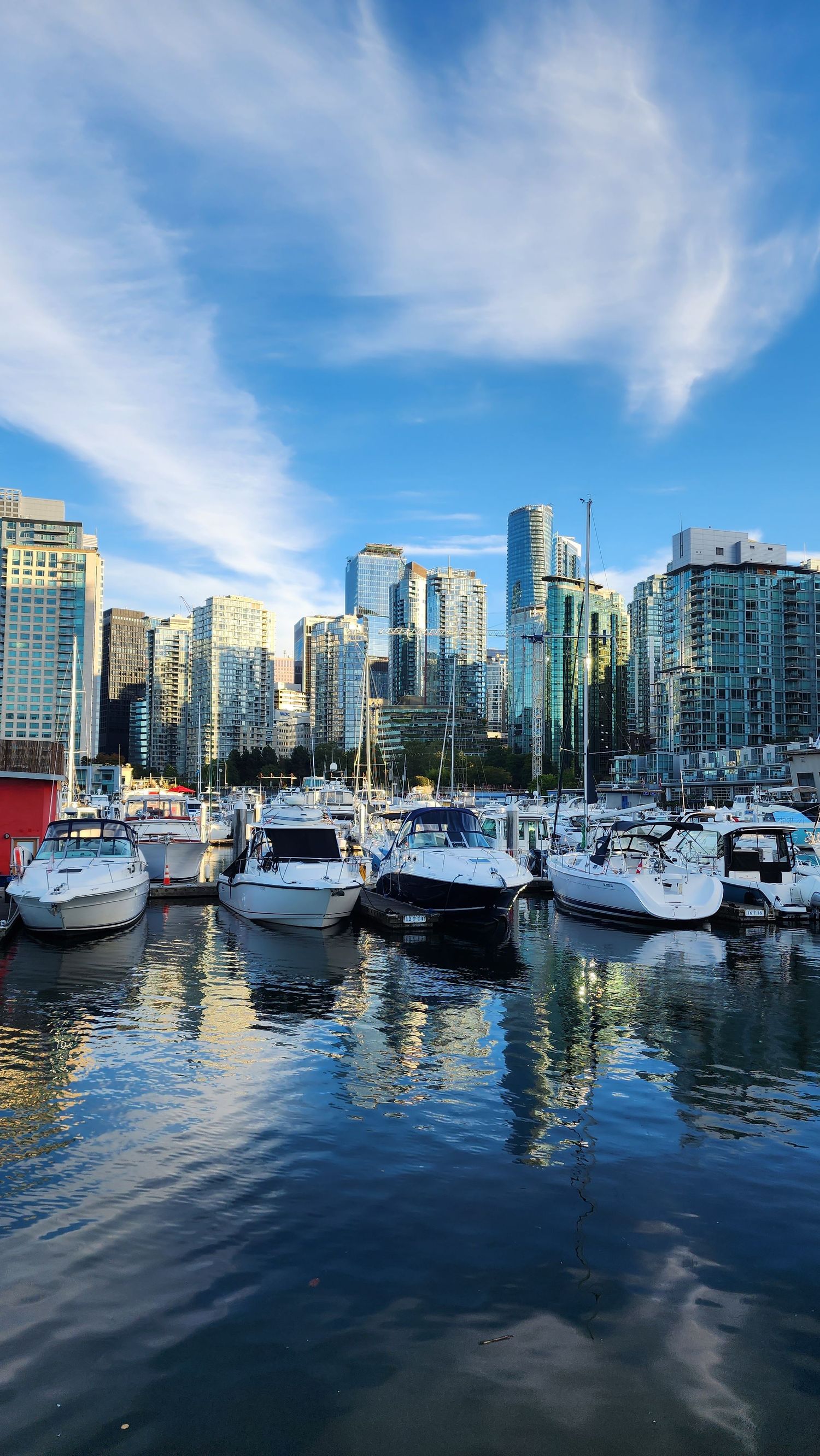 Yachts and boats docked at Vancouver marina with city skyline and blue sky reflections.