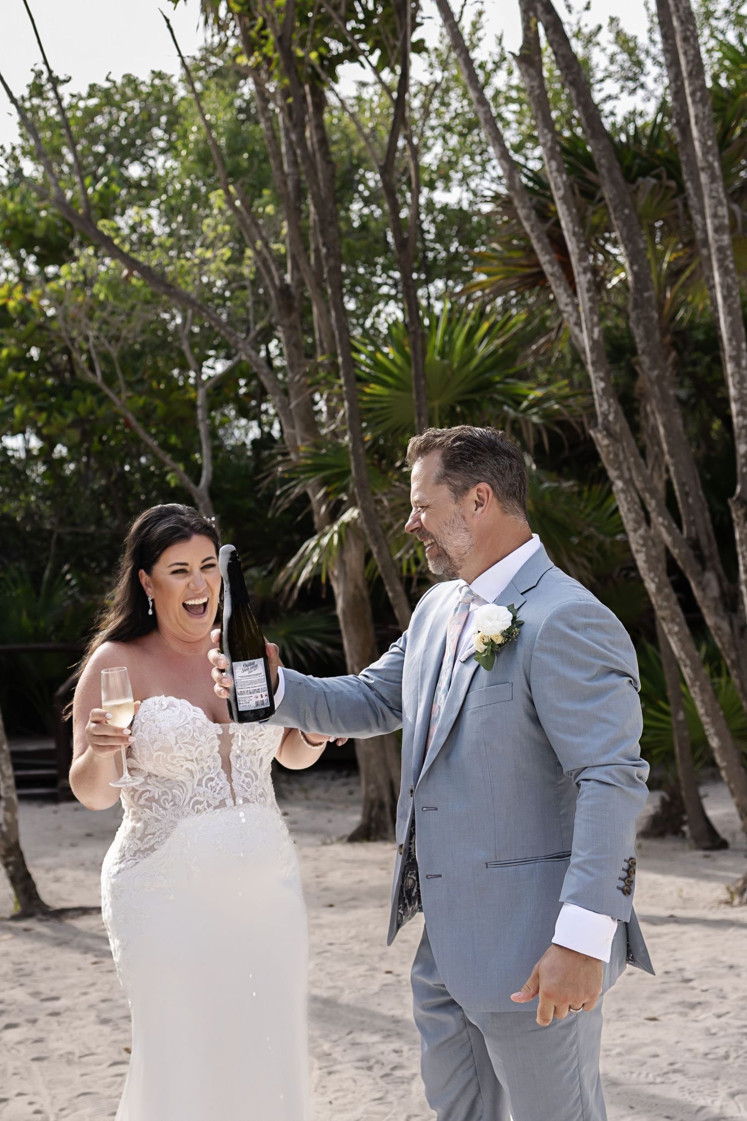 Couple sharing a joyful first look moment on a beach with palm trees and natural scenery in the background.
