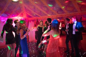 Wedding guests dancing together on a pink-lit dance floor at an evening reception celebration.