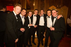 A group of men in black tuxedos and bow ties smile and laugh together at a formal event.