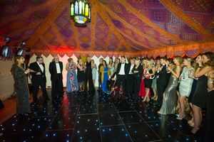 Party guests dancing on a glowing black dance floor under decorative fabric draping and a Moroccan lantern.
