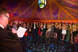 Party guests dance and celebrate under a tent decorated with colourful lights and fabric draping.