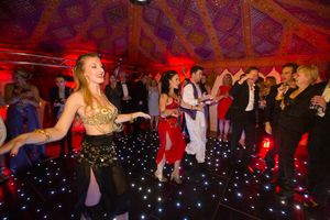 People dancing and celebrating at a party with a glowing dance floor under red lighting in an ornate tent venue.