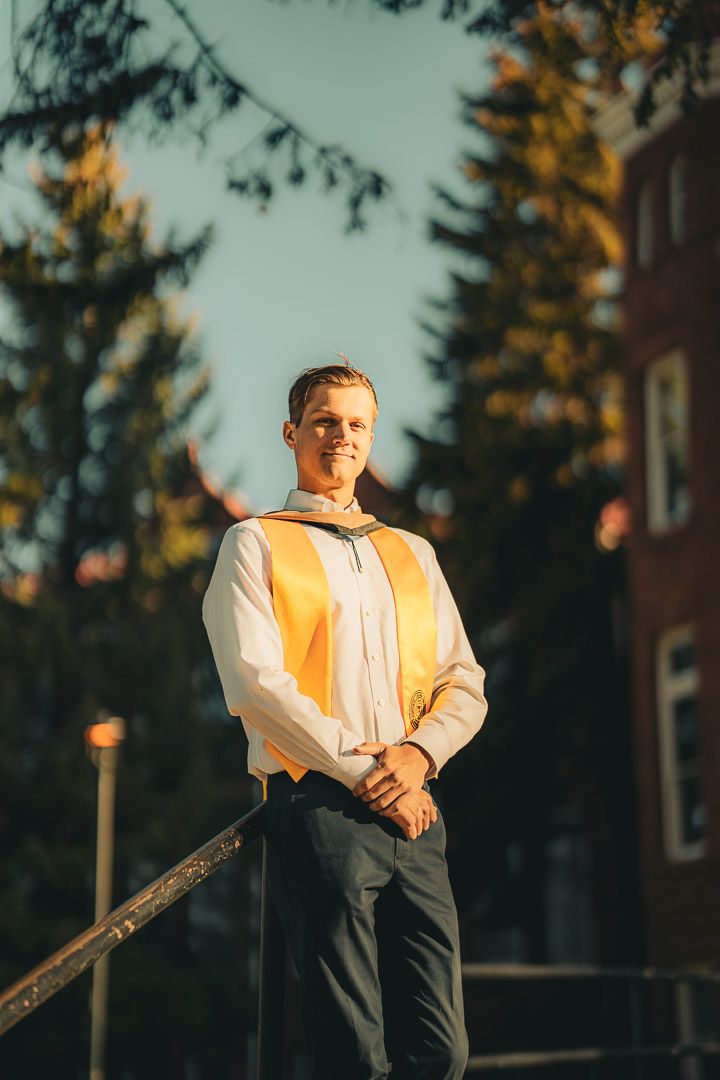 Person in white shirt and dark pants stands in warm golden sunlight against wooded backdrop during sunset.