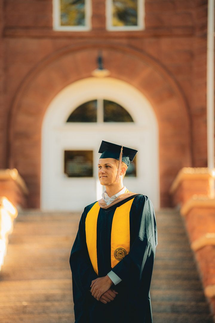 Graduate in black and gold regalia poses for portraits in front of historic brick architecture.
