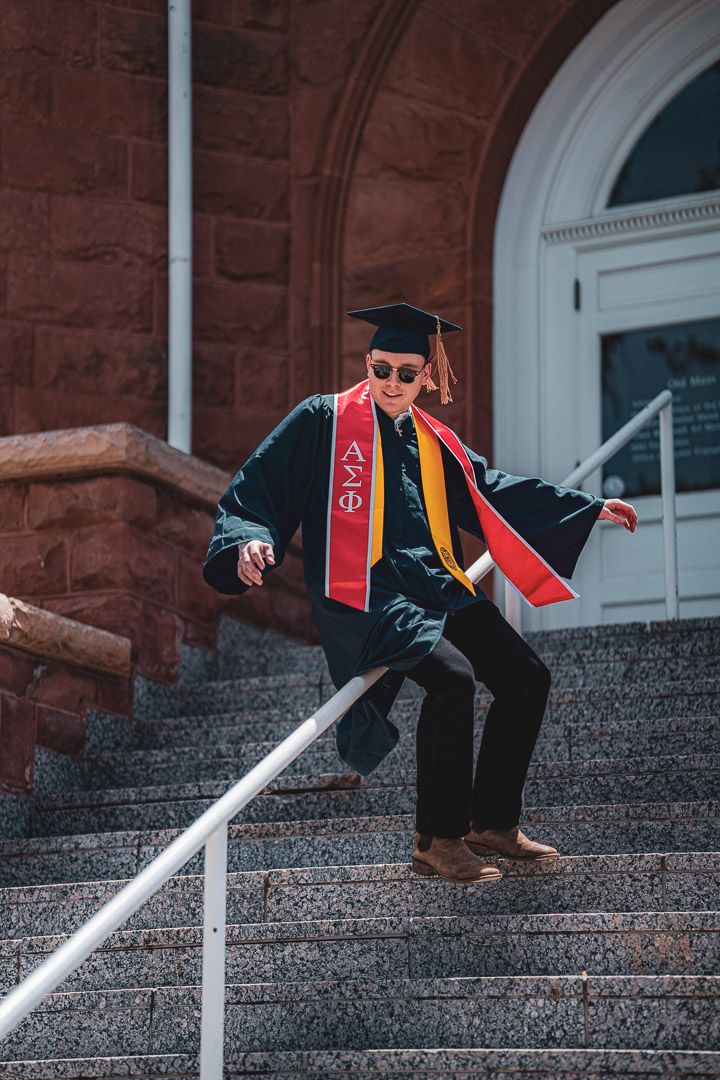 Graduation photoshoot sequence showing a graduate sliding down a handrail in their cap and gown with colorful stoles.