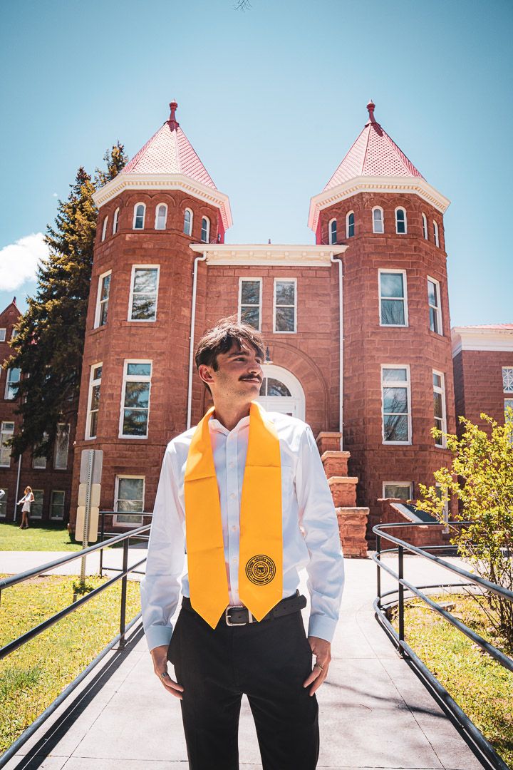Graduate poses in front of red brick university building with twin towers.