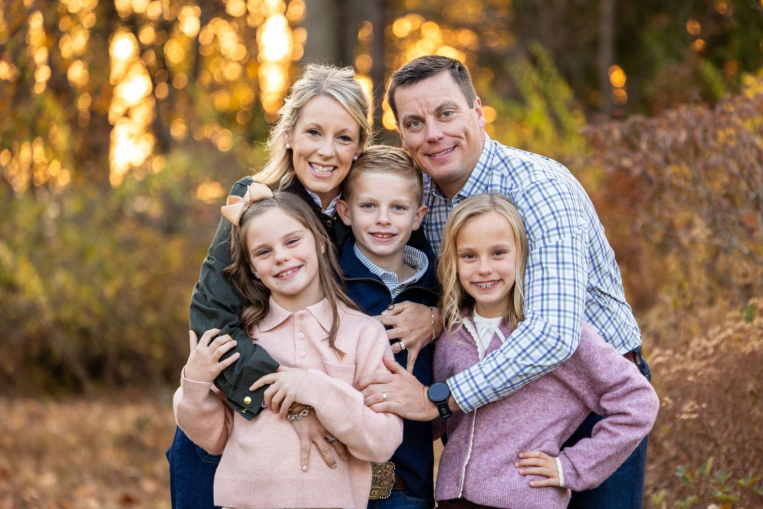 Family walking together and holding hands in a sunny meadow with golden fall foliage during sunset.