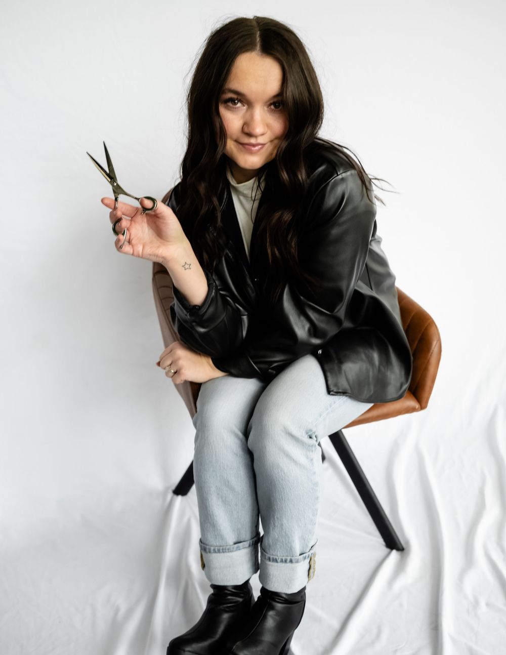 Model wearing leather jacket and jeans poses casually on white background.