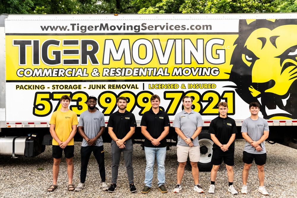 Group of movers posing in front of yellow branded Tiger Moving company truck.